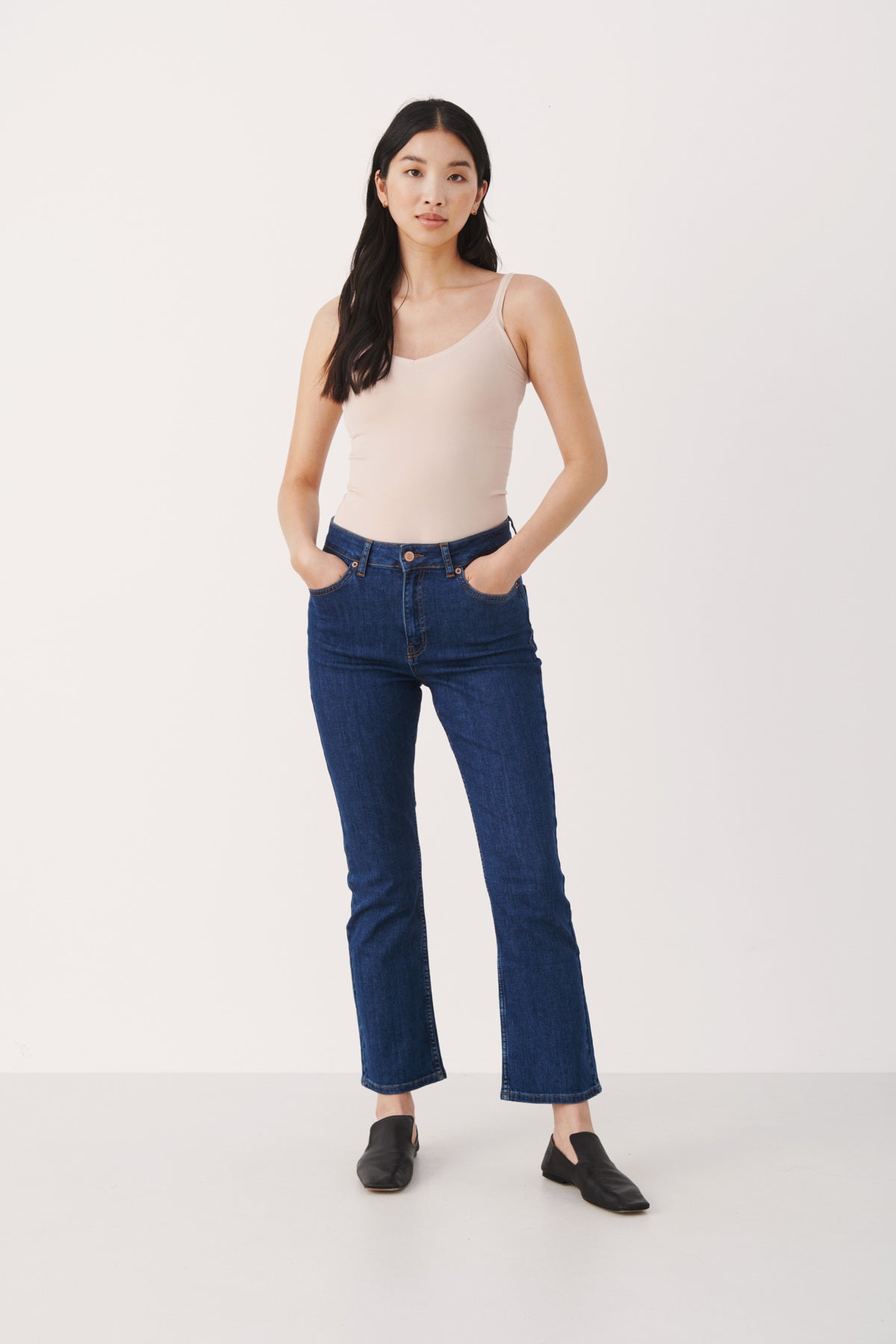 Woman wearing a beige tank top and blue jeans on a white background