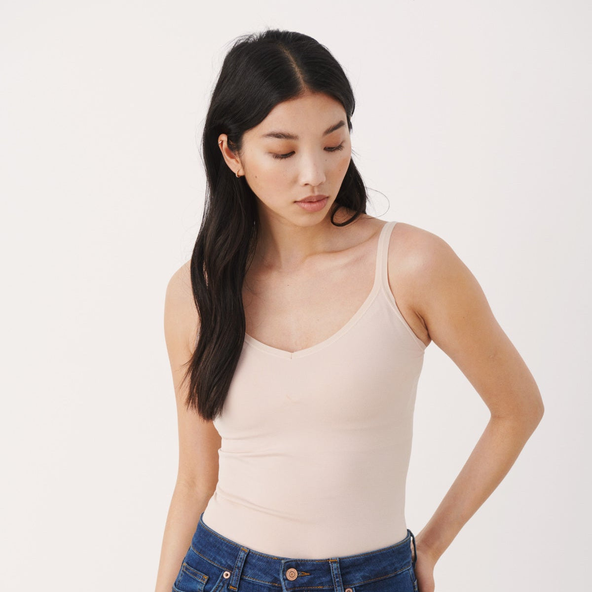 Woman wearing a beige tank top and blue jeans on a white background
