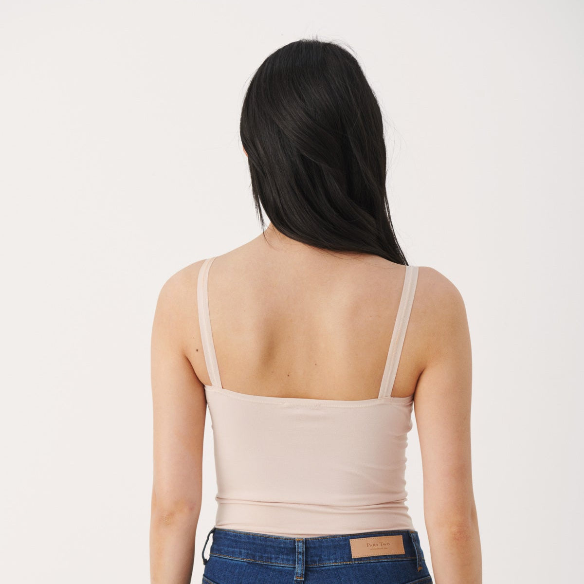 Woman wearing a beige tank top and blue jeans on a white background