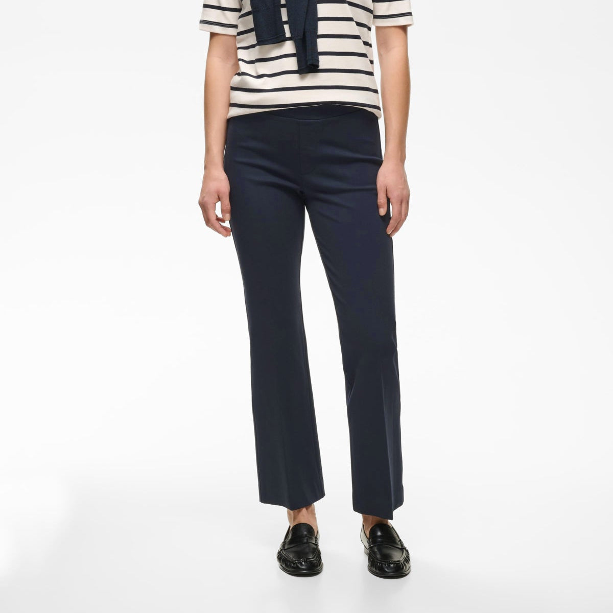 A woman modeling a short-sleeve navy and cream striped top with a navy necktie, paired with navy trousers and black loafers, against a plain white studio background.