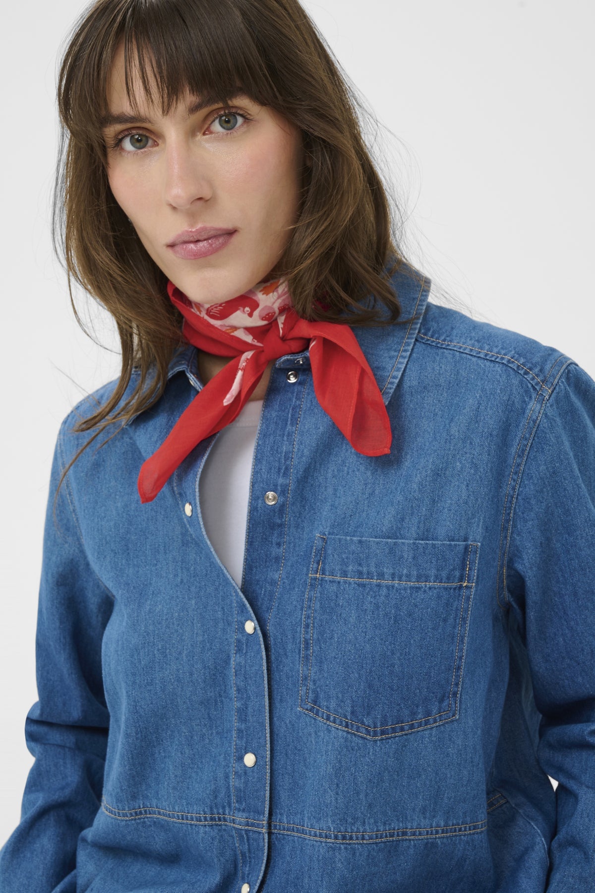 Woman wearing a blue denim shirt and red scarf against a white background