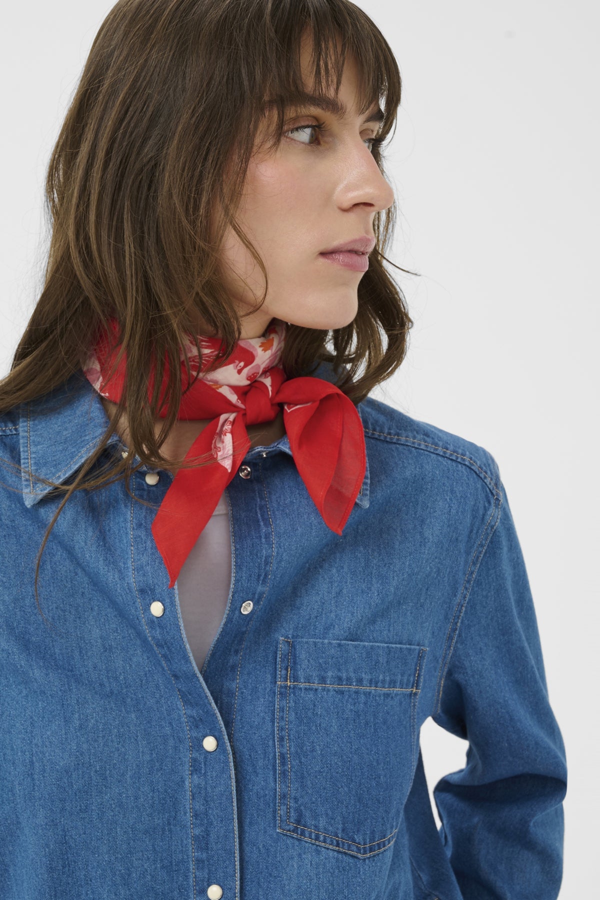 Woman wearing a red scarf and blue denim shirt against a white background