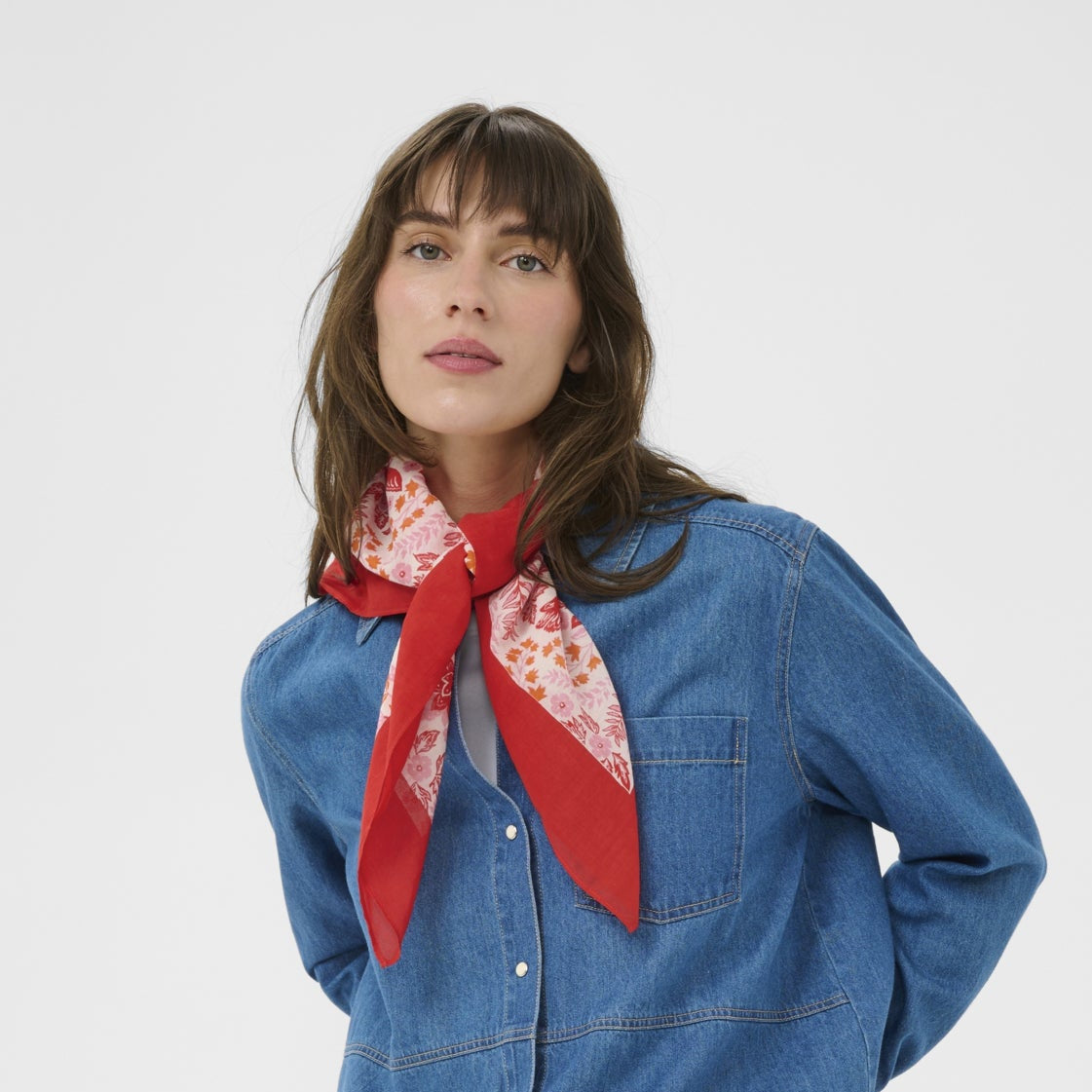 Woman wearing a blue denim shirt with a red scarf on a white background
