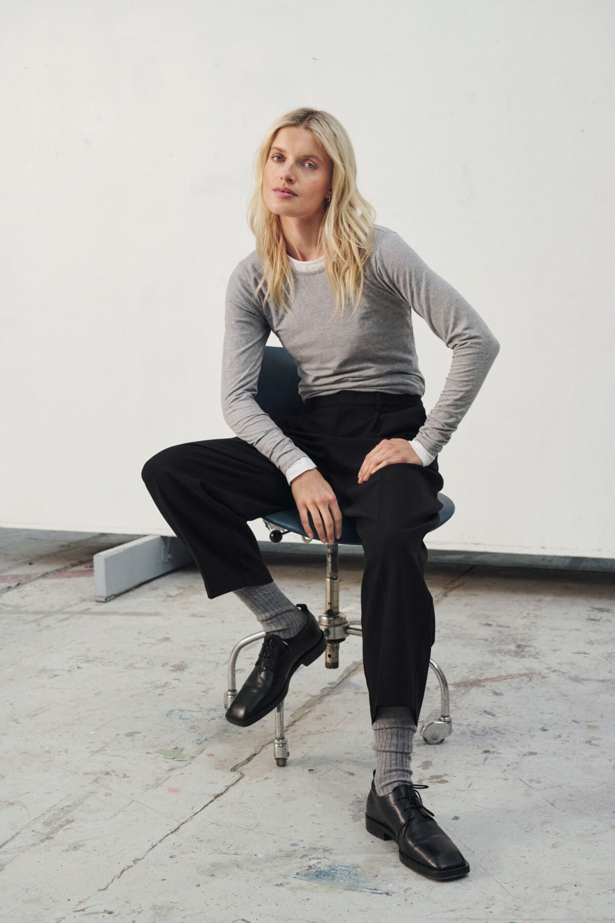 Person sitting on a chair wearing a gray long-sleeve shirt, black pants, and black shoes.