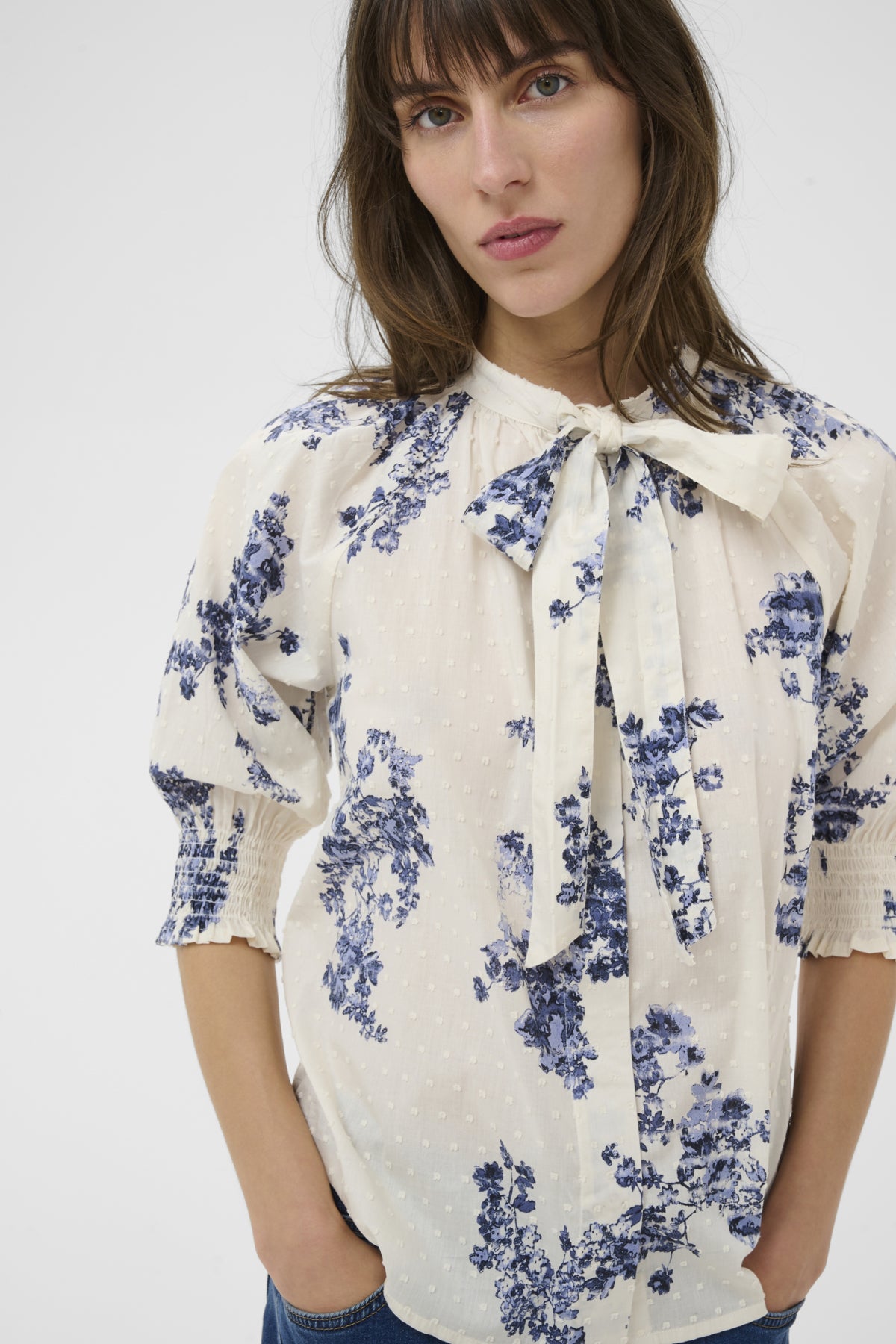 Woman wearing a white blouse with blue floral patterns and a bow neckline on a white background