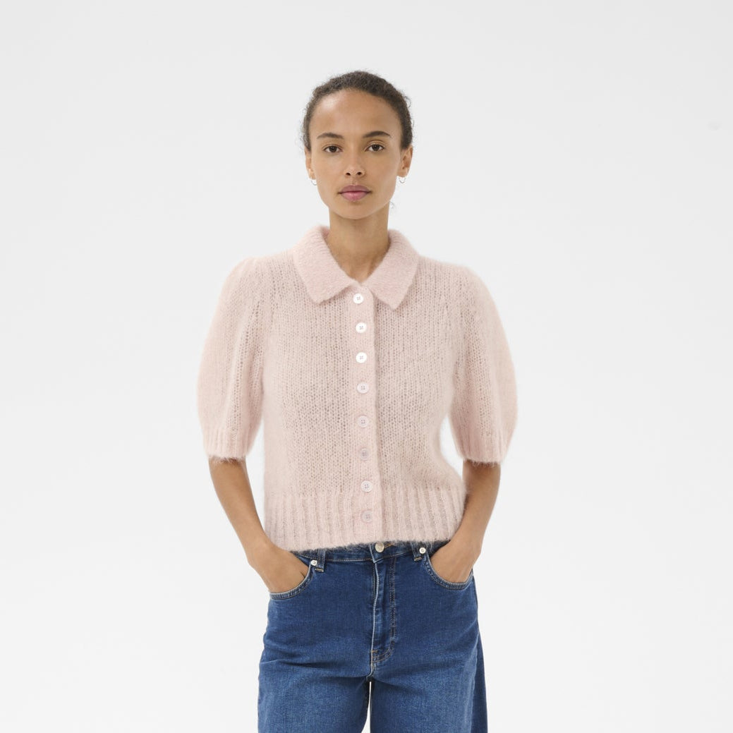 Person wearing a light pink knitted cardigan, blue jeans, and brown shoes on a white background