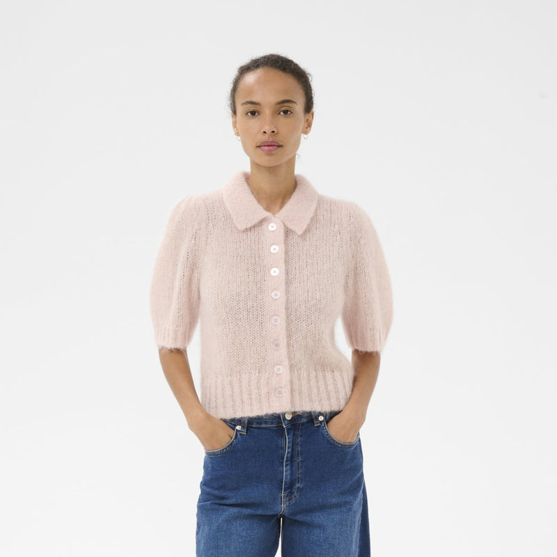 Person wearing a light pink knitted cardigan, blue jeans, and brown shoes on a white background