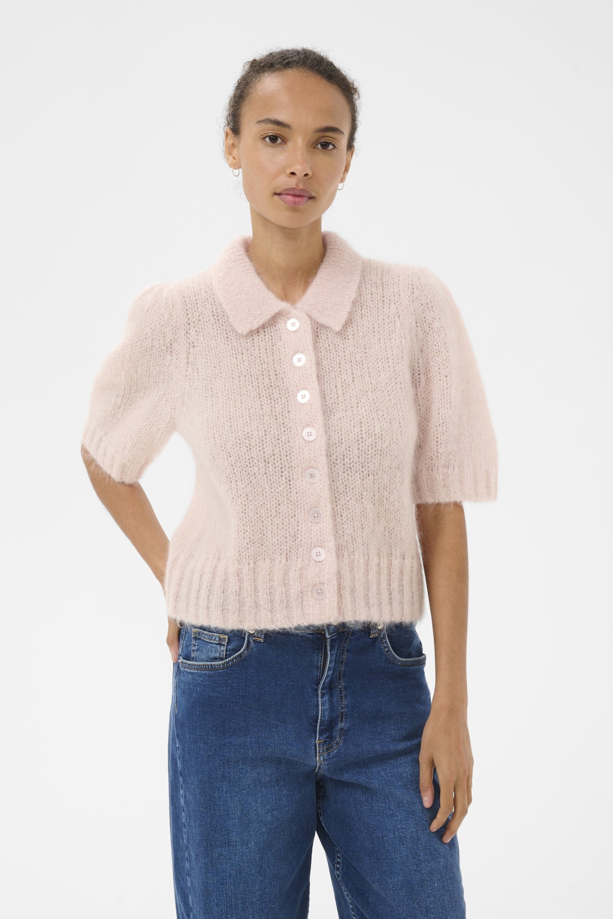 Woman wearing a light pink knitted cardigan and blue jeans on a white background