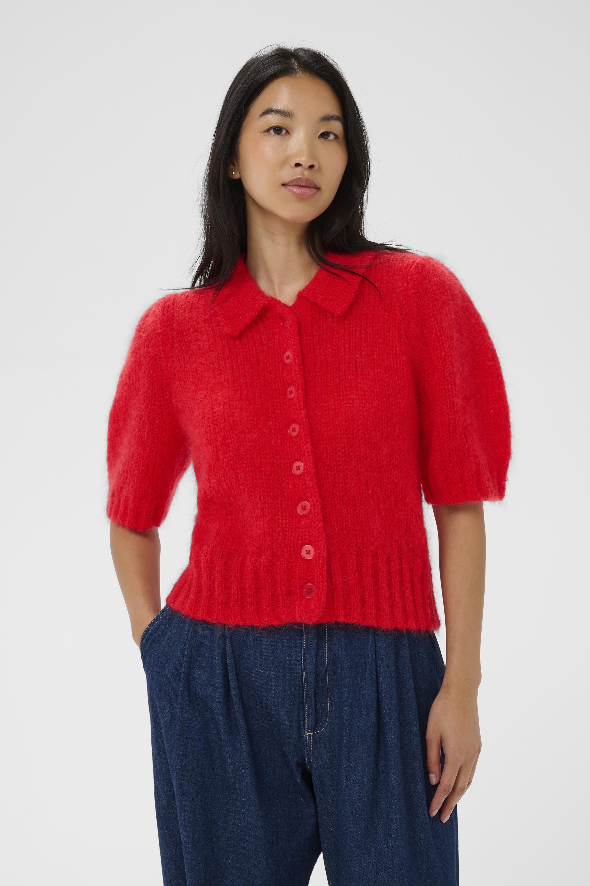 Woman wearing a red knitted cardigan and blue pants on a white background