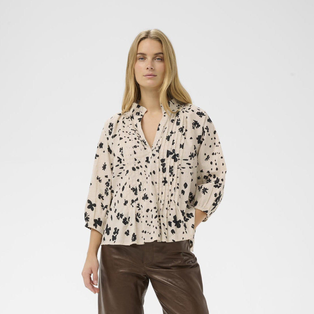 Woman wearing a patterned blouse and brown pants on a white background