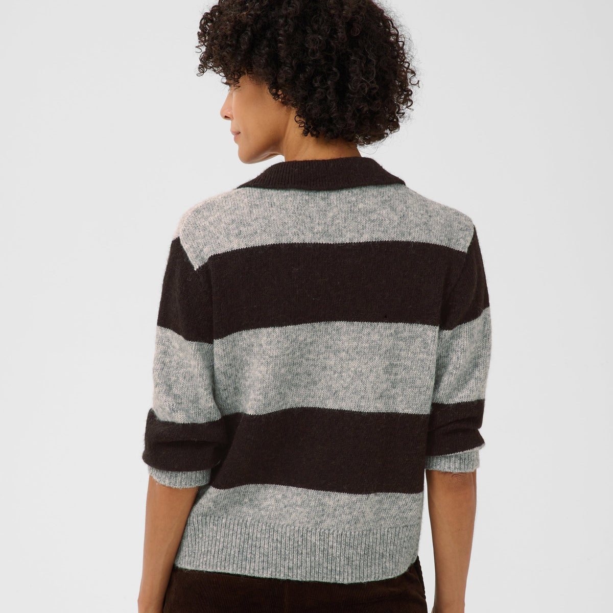 A woman shown from the back wearing a knit sweater with wide horizontal stripes in dark brown and light heather gray, against a plain light gray studio background.