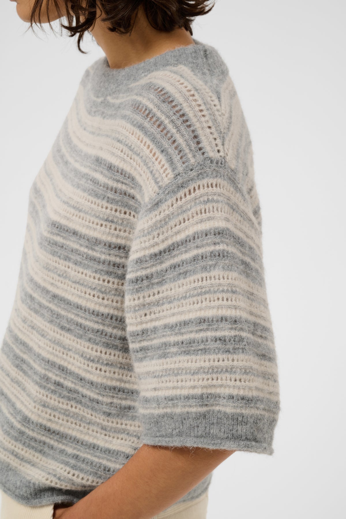Close-up of a person wearing a fuzzy knit sweater with horizontal gray and off-white stripes, cropped from the side against a plain light background.