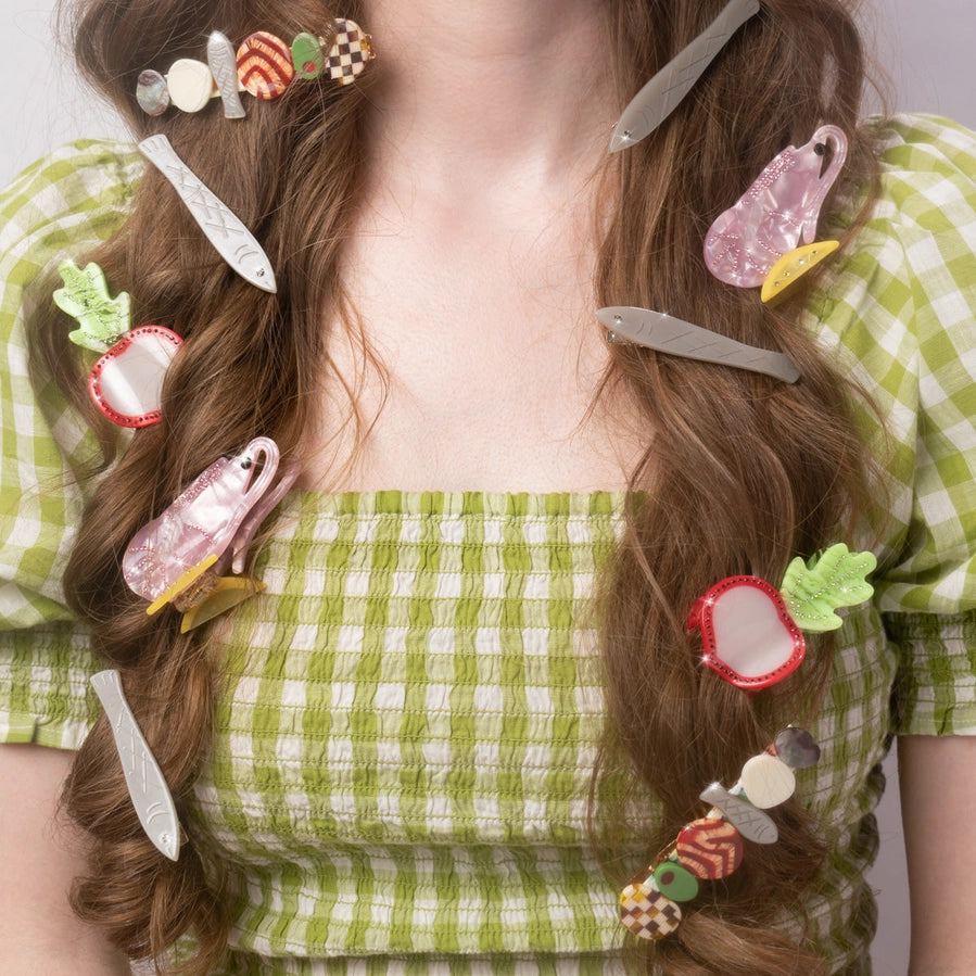 Person is modelling many food themed colorful hair clips in their hair wearing a green checkered dress.