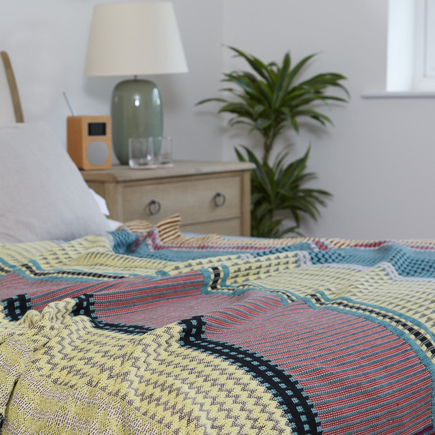 Multicolored woven throw blanket with textured stripes and geometric patterns in shades of yellow, teal, red, and black.