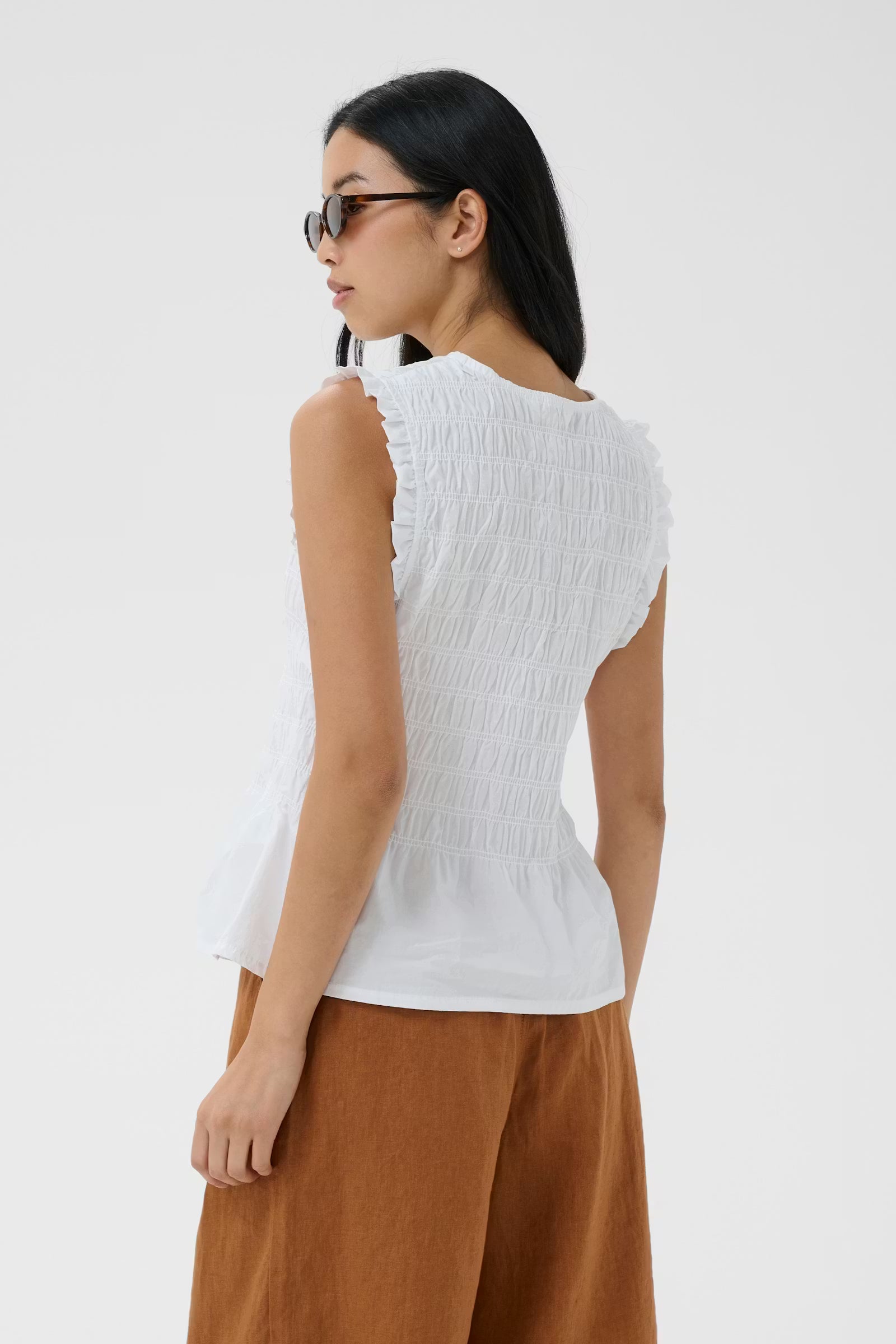 Woman wearing a white sleeveless top and brown pants on a white background