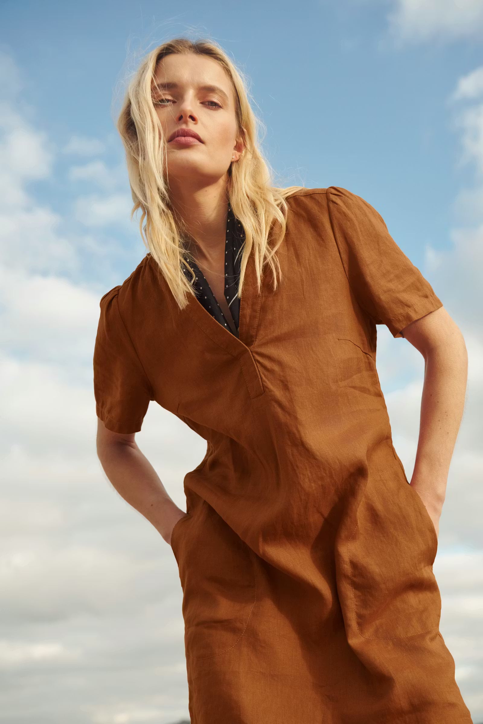 Woman wearing a brown dress against a blue sky with clouds