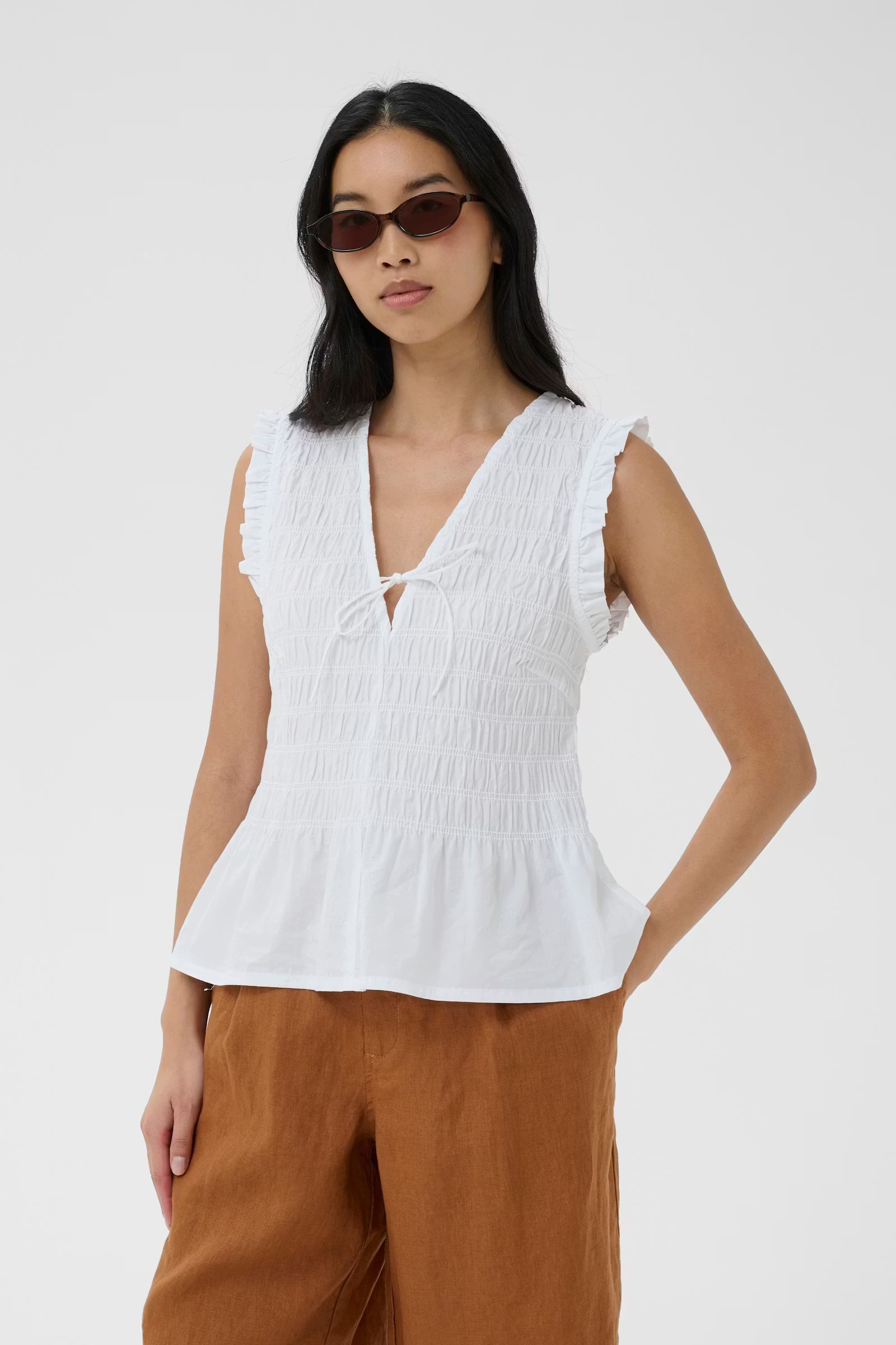 Woman wearing a white sleeveless top and brown pants on a white background