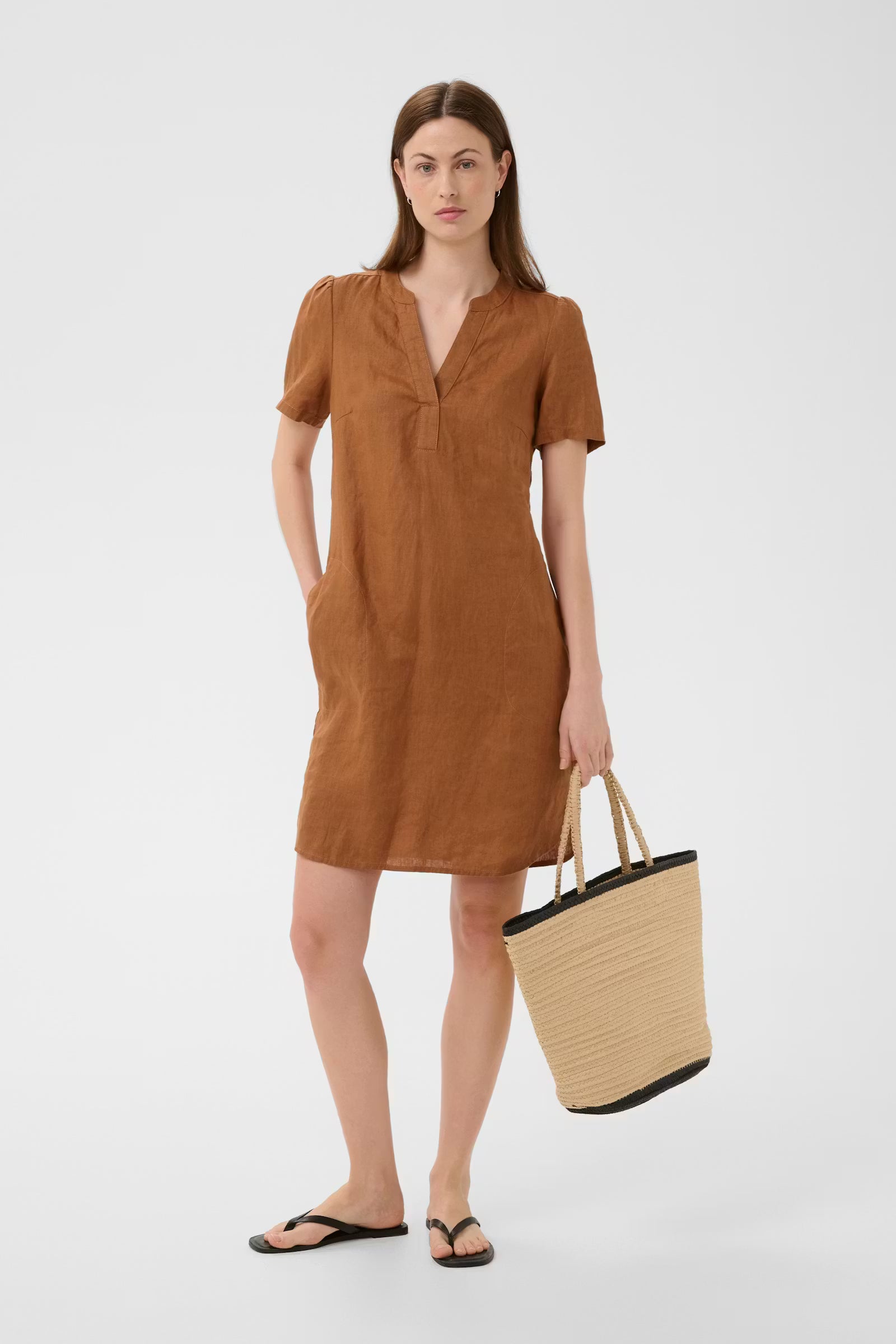 Woman wearing a brown dress holding a straw bag on a white background