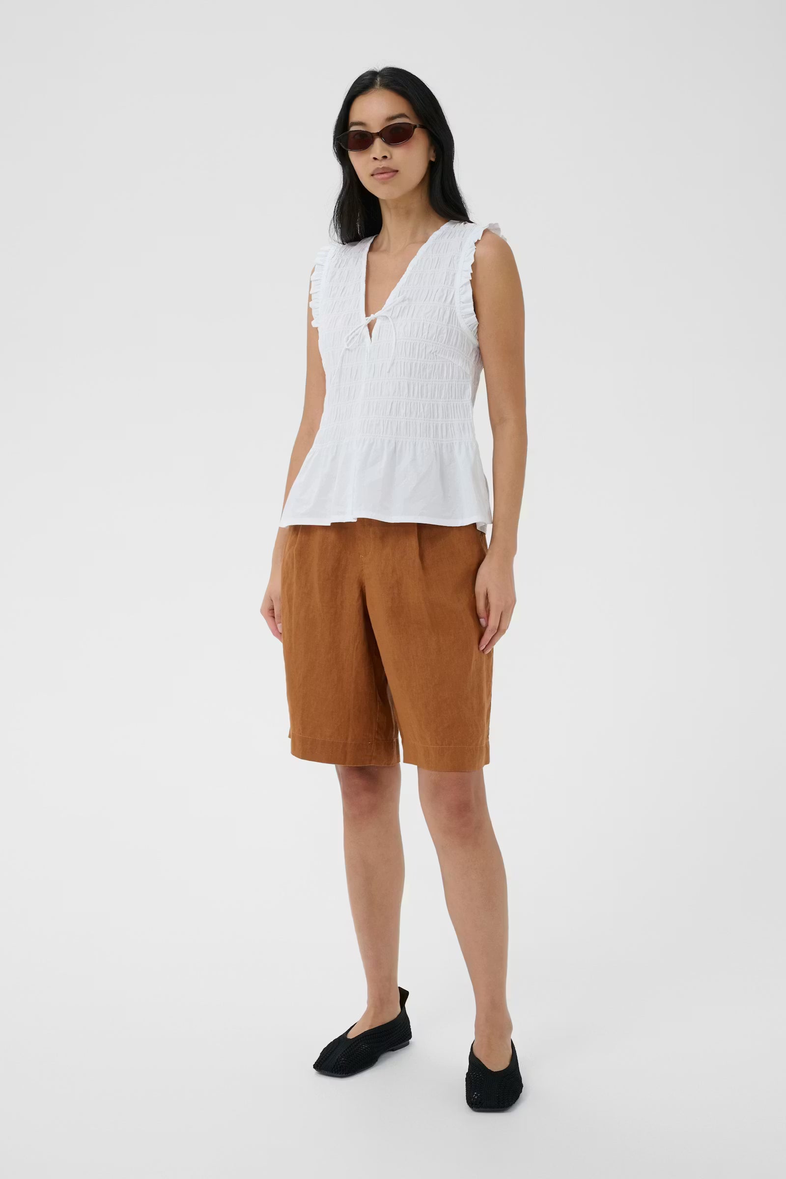 Woman wearing a white sleeveless top and brown shorts on a white background
