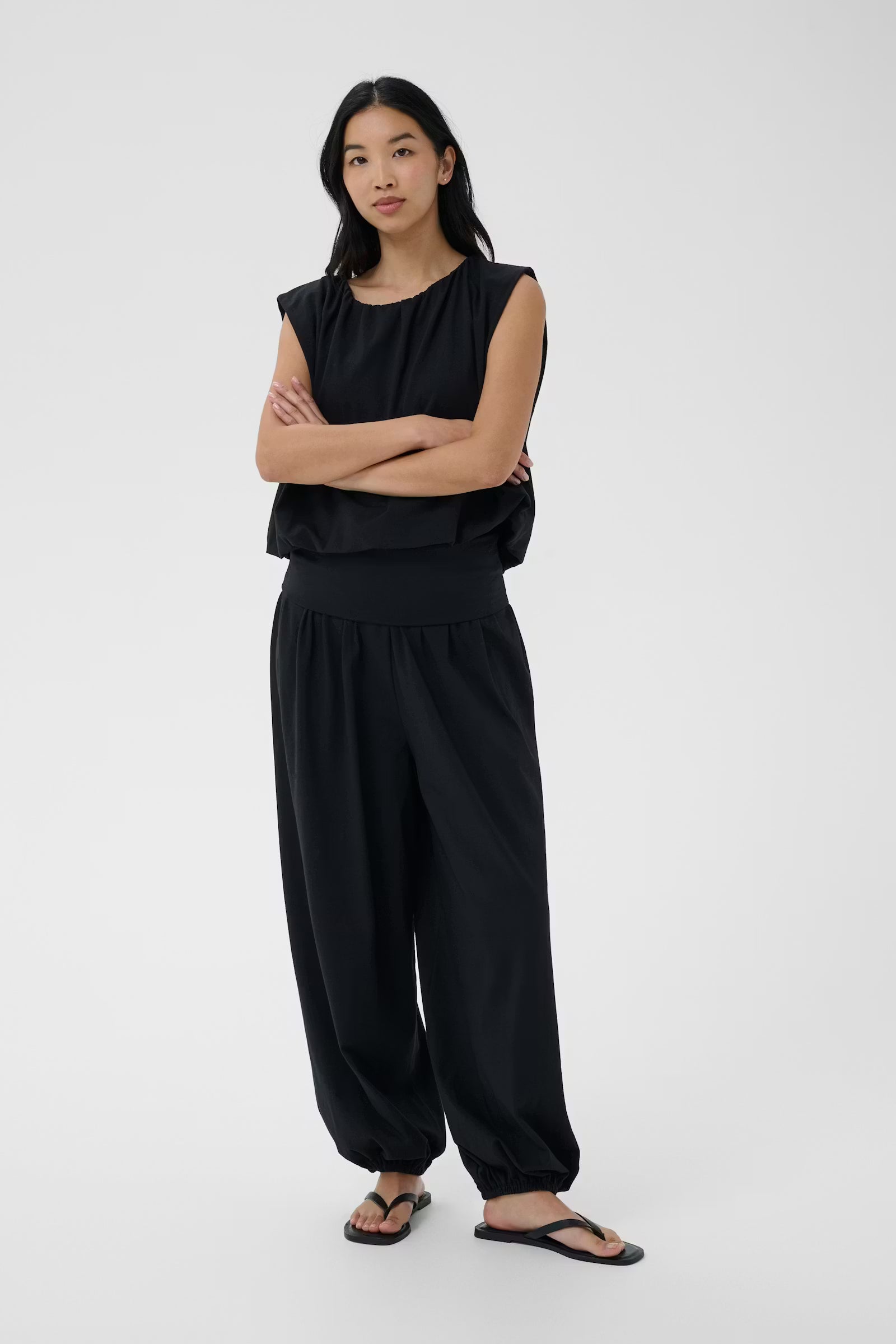 Person wearing a black sleeveless top and wide-leg pants on a white background