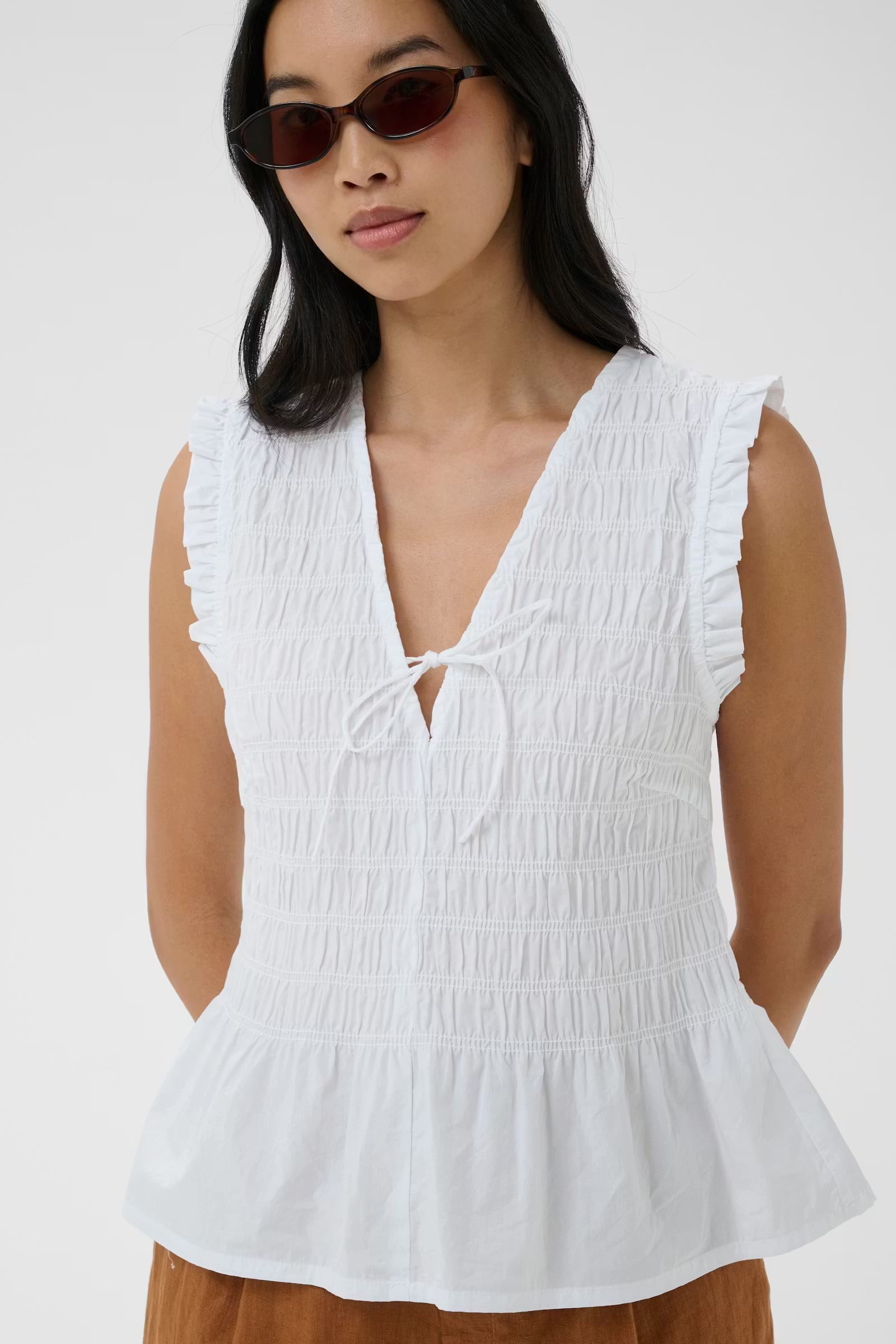 Woman wearing a white sleeveless top with ruffled details on a plain background