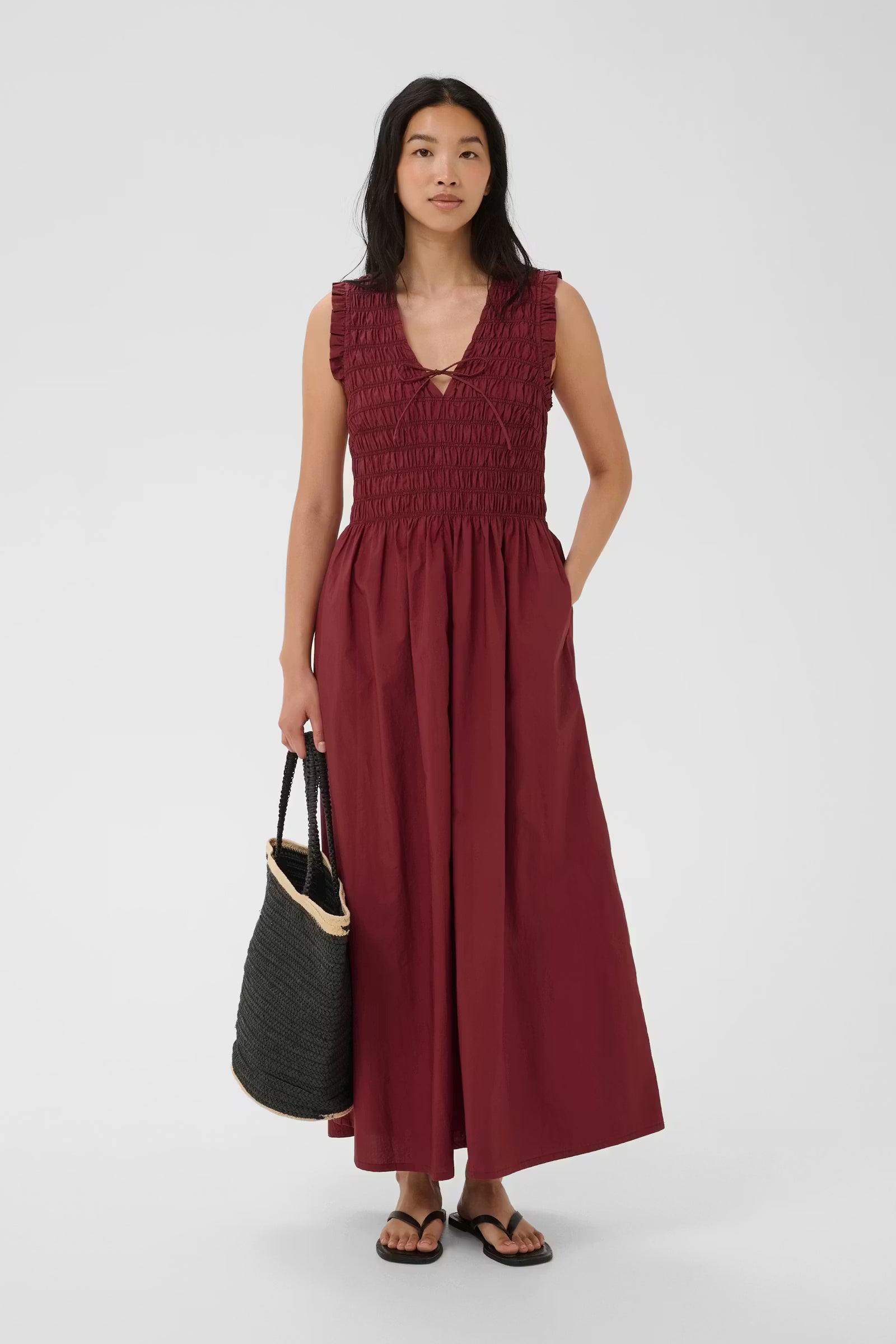 Woman wearing a burgundy dress holding a black bag on a white background