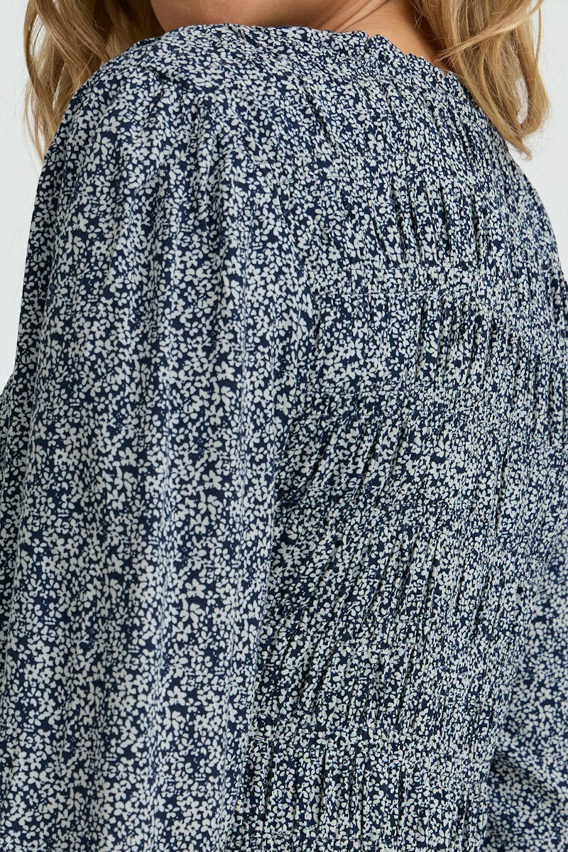 Close-up of a person wearing a blue floral patterned blouse against a white background