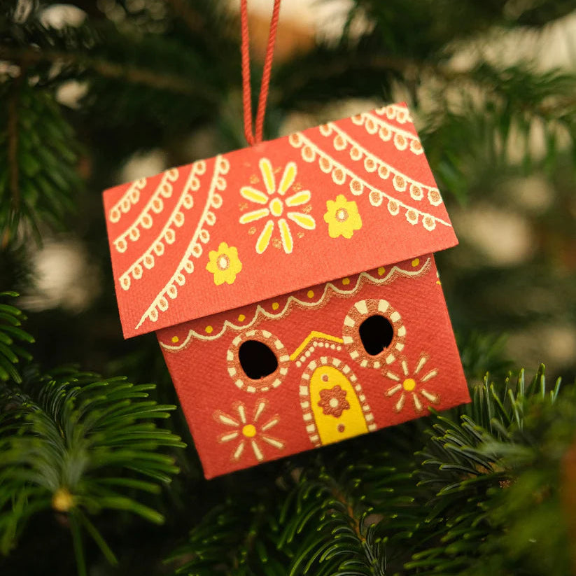 Decorative red birdhouse ornament hanging on a Christmas tree.
