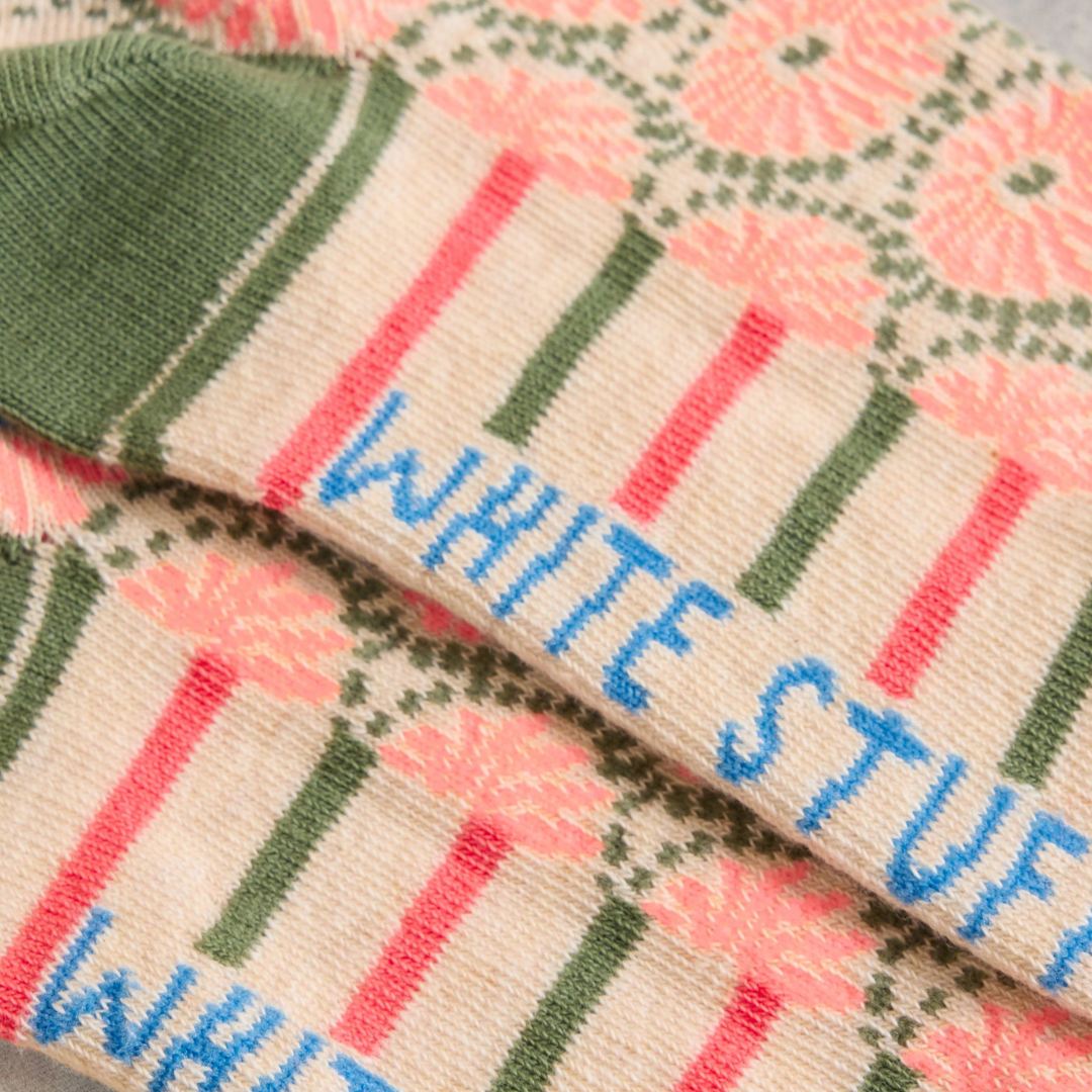 Cream-colored socks with pink floral pattern, green and red stripes, and "WHITE STUFF" knit in blue.