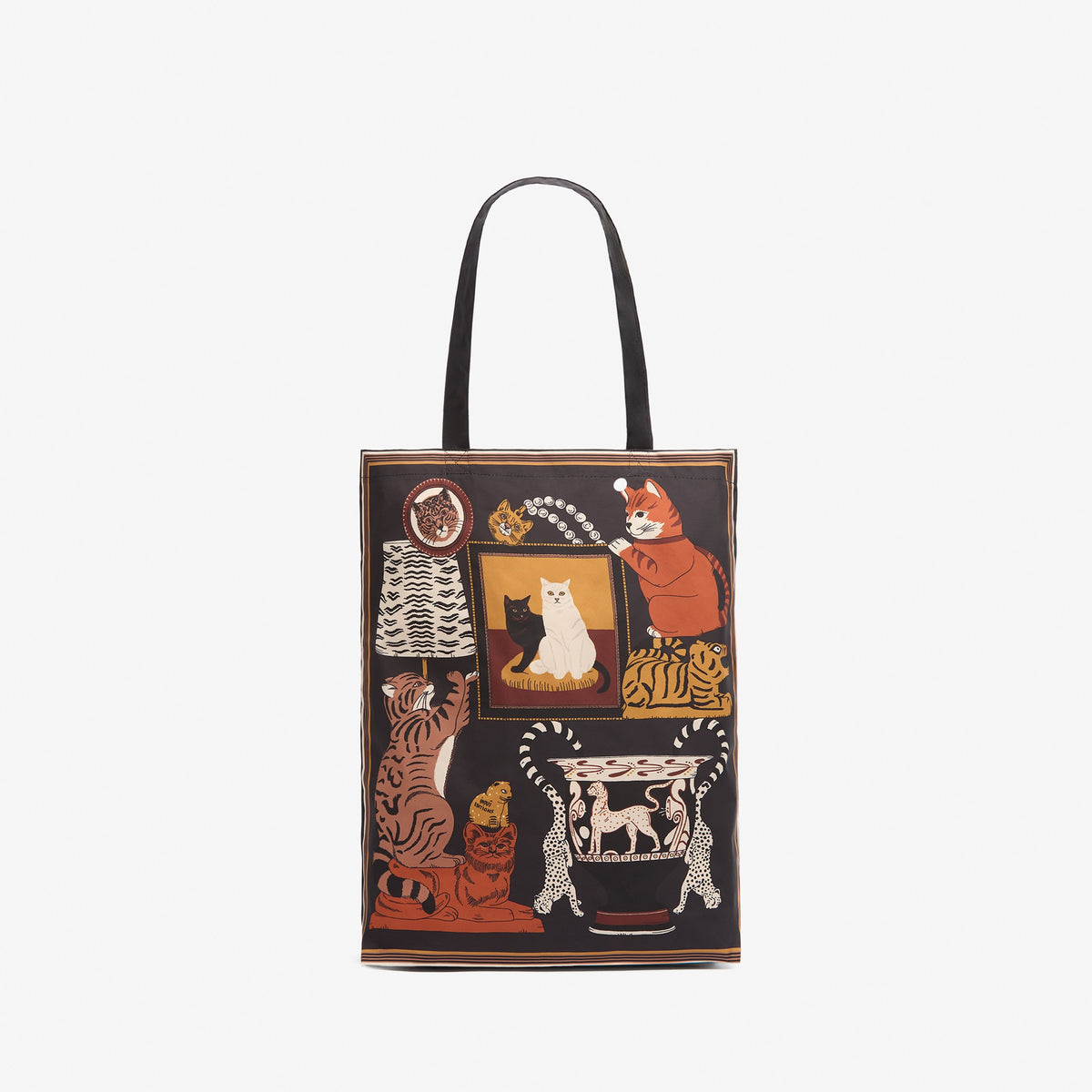A black canvas tote bag featuring a whimsical collage of illustrated cats in various poses and settings, including a mirror, a lamp, and a table, with black shoulder straps, shown against a plain white background.