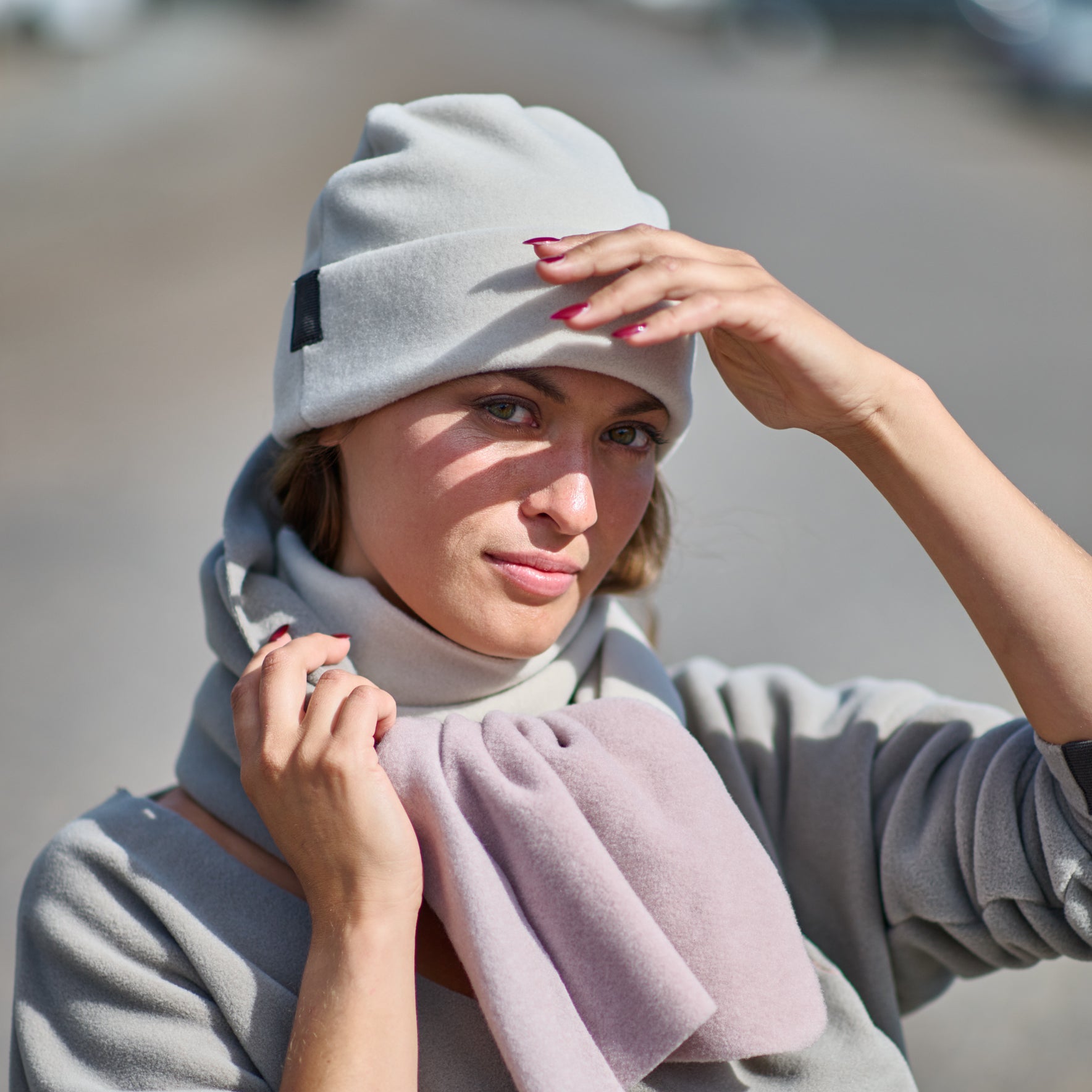 Woman wearing a gray beanie and coat with a pink scarf, standing outdoors.