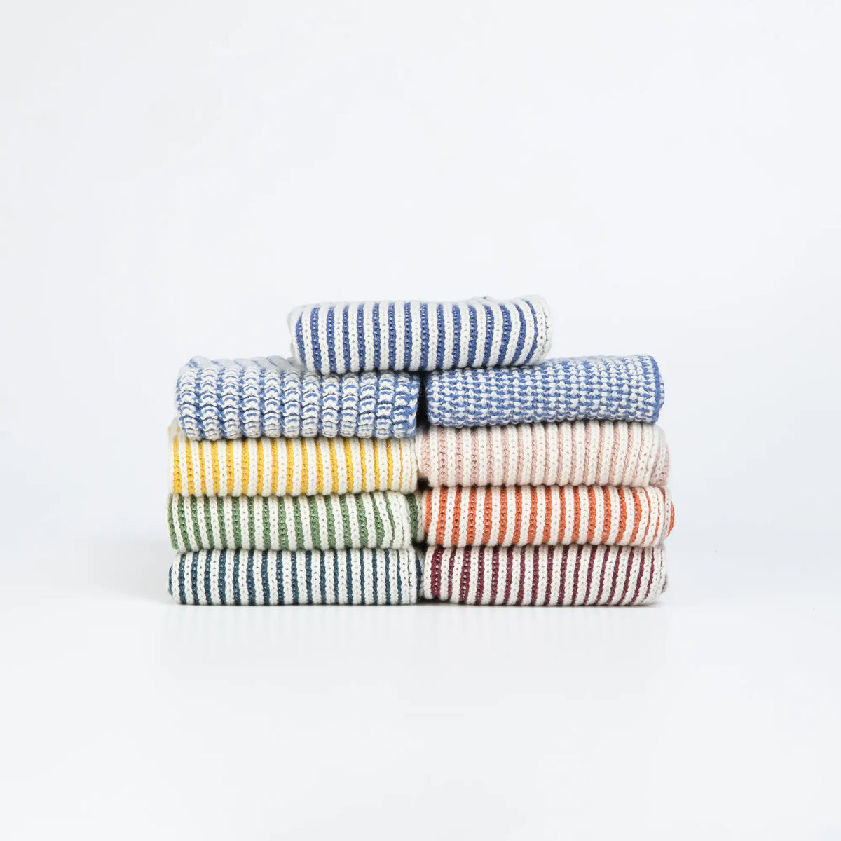 A stack of eight folded striped kitchen towels in various colors, including blue, yellow, green, beige, orange, and red, arranged neatly on a white background.