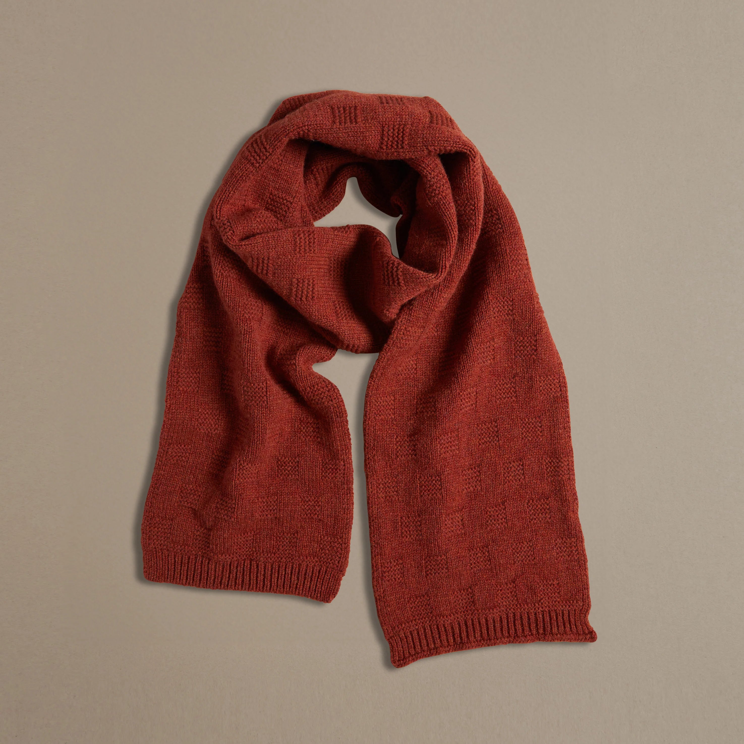 Rust-colored knitted wool scarf with a textured pattern.