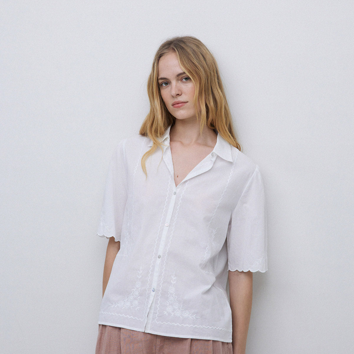 White embroidered cotton shirt with short, scalloped sleeves and button-front closure.