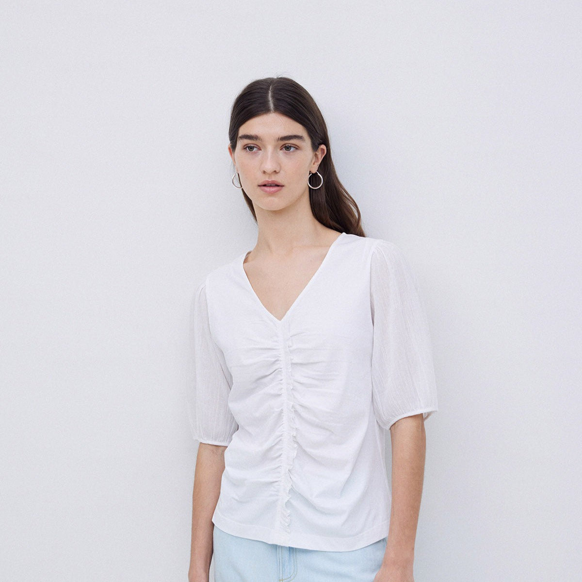 White v-neck, short-sleeve top with ruched detail at the center.