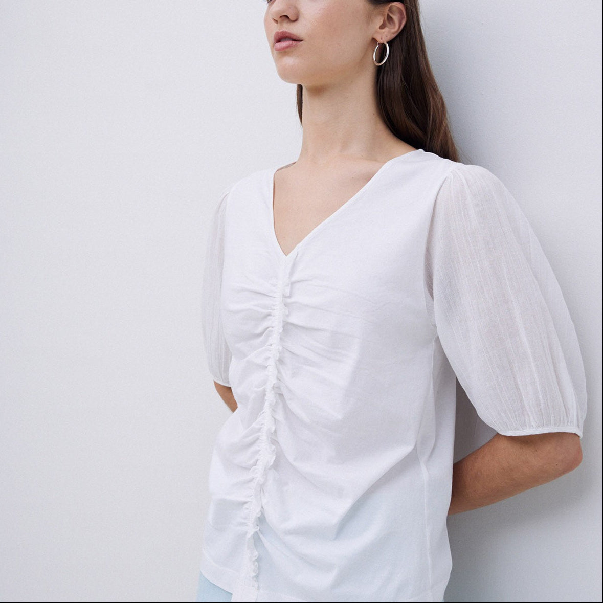 White v-neck, cinched-waist, short-sleeve blouse with sheer puff sleeves.