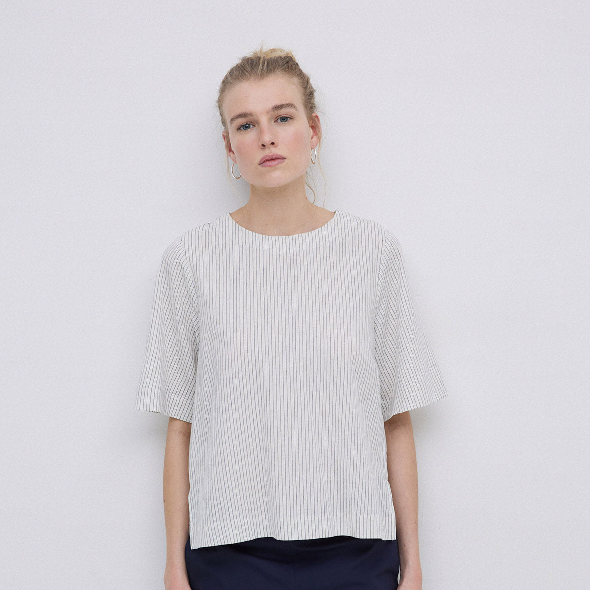 Cream-colored linen top with thin, dark vertical stripes, short sleeves, and a boxy fit.