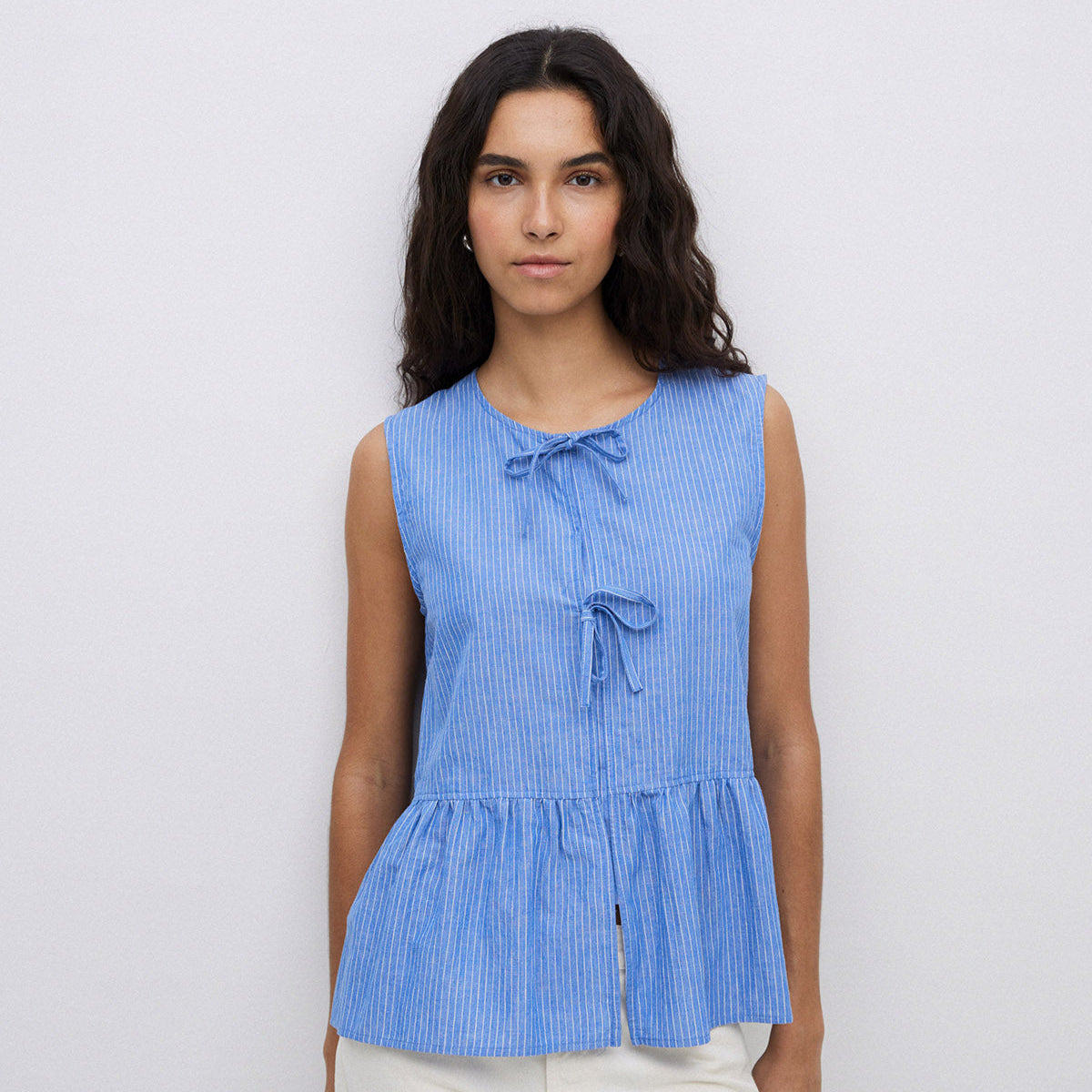 Blue sleeveless linen top with thin white stripes and a tie detail at the center.  The top has a peplum hem.