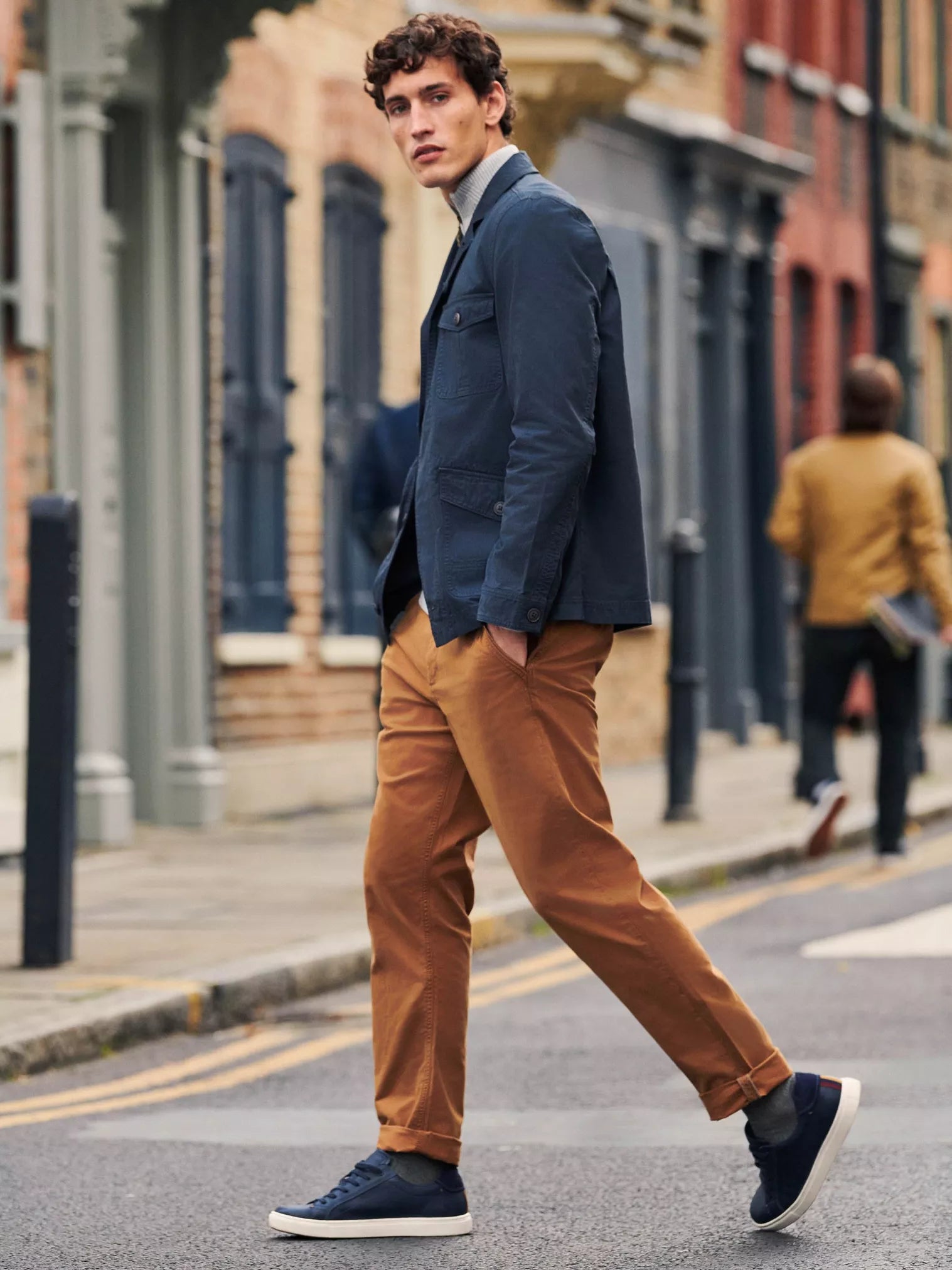 Man wearing a navy blue jacket, mustard chinos, and dark blue sneakers.