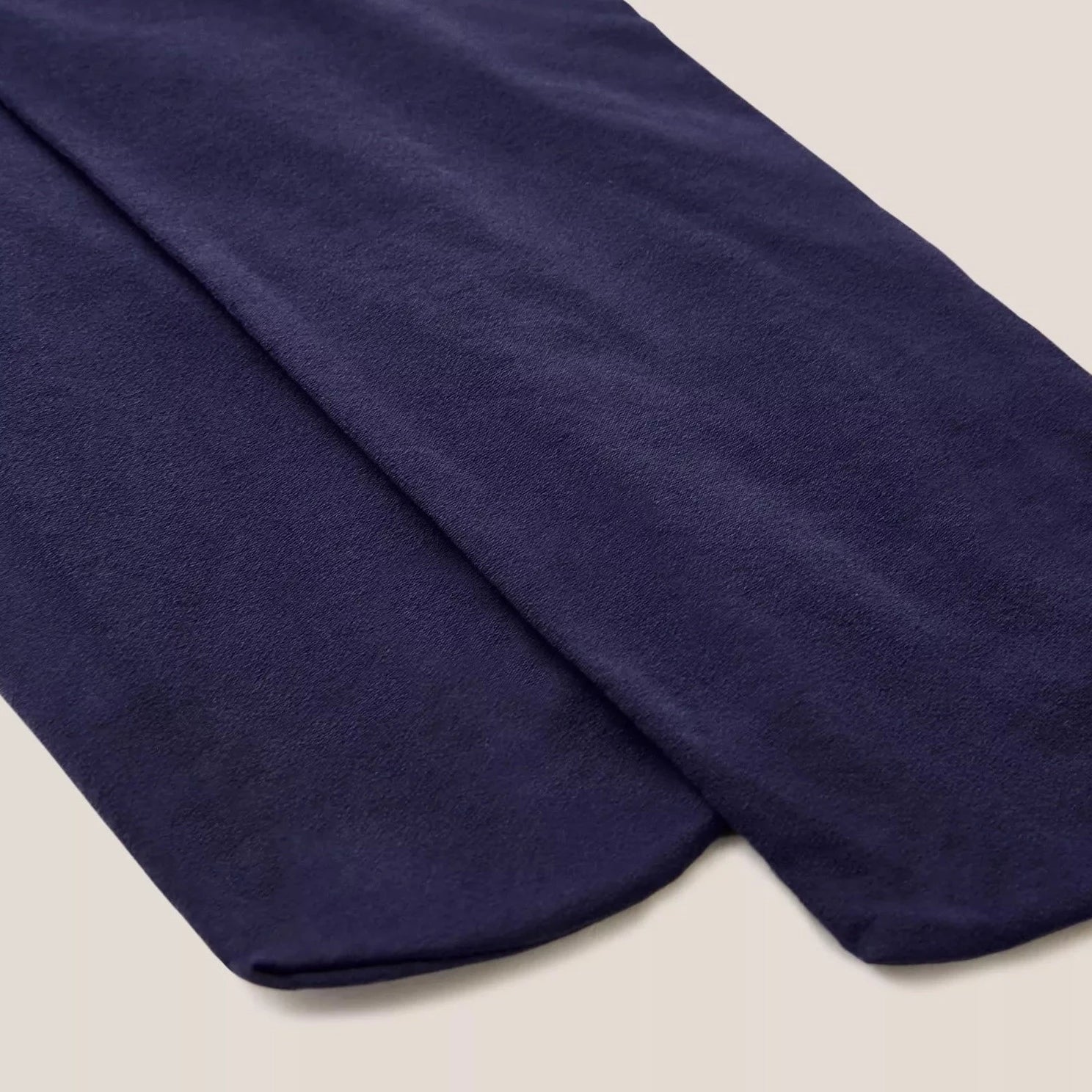 Pair of dark navy blue opaque tights folded on a light beige background.
