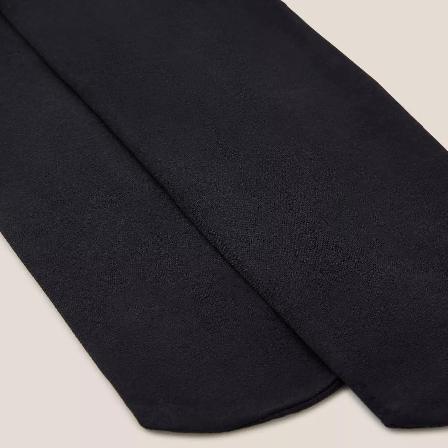 Pair of dark navy blue opaque tights folded on a light beige background.