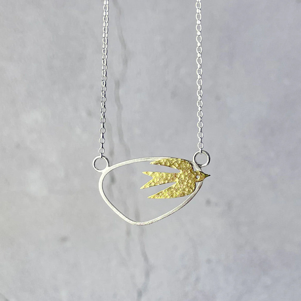 Necklace with a gold and silver bird-shaped pendant on a light gray background