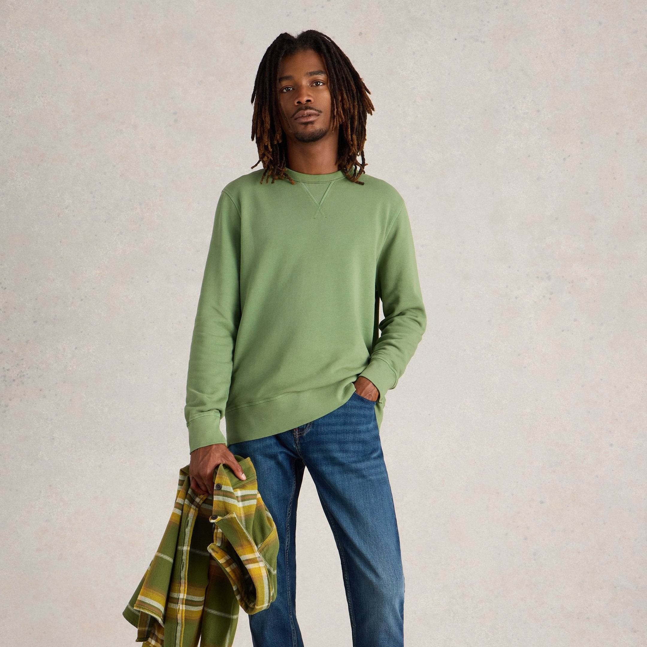 Sage green crewneck sweatshirt with long sleeves. Model also wears blue jeans and holds a plaid shirt.