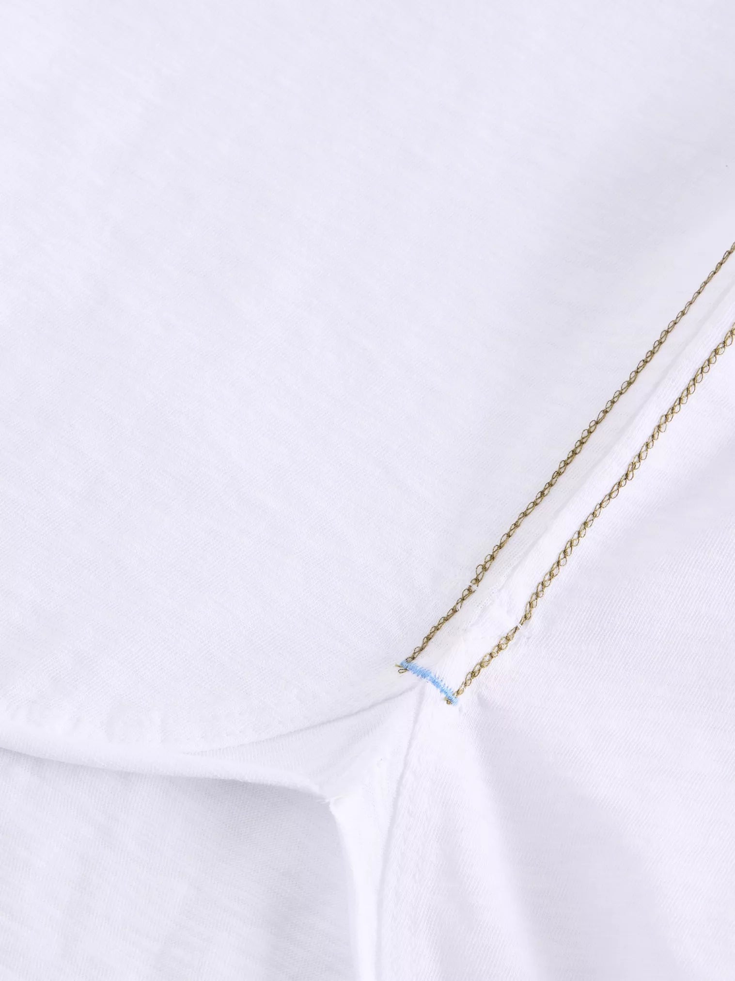 Close-up of white fabric with gold chain stitching detail and a light blue accent stitch.