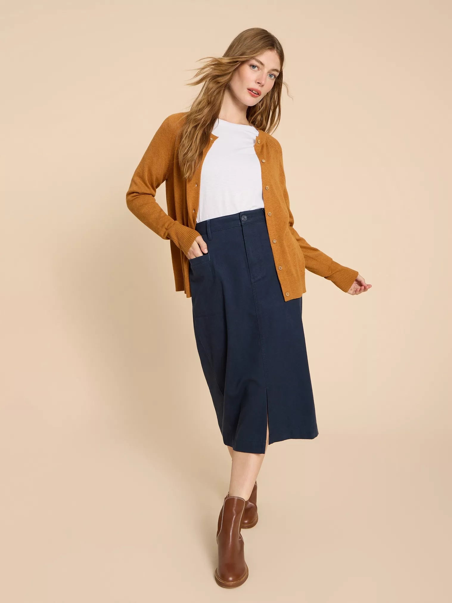 Dark navy midi skirt with front slit and pockets, paired with a mustard-colored cardigan.
