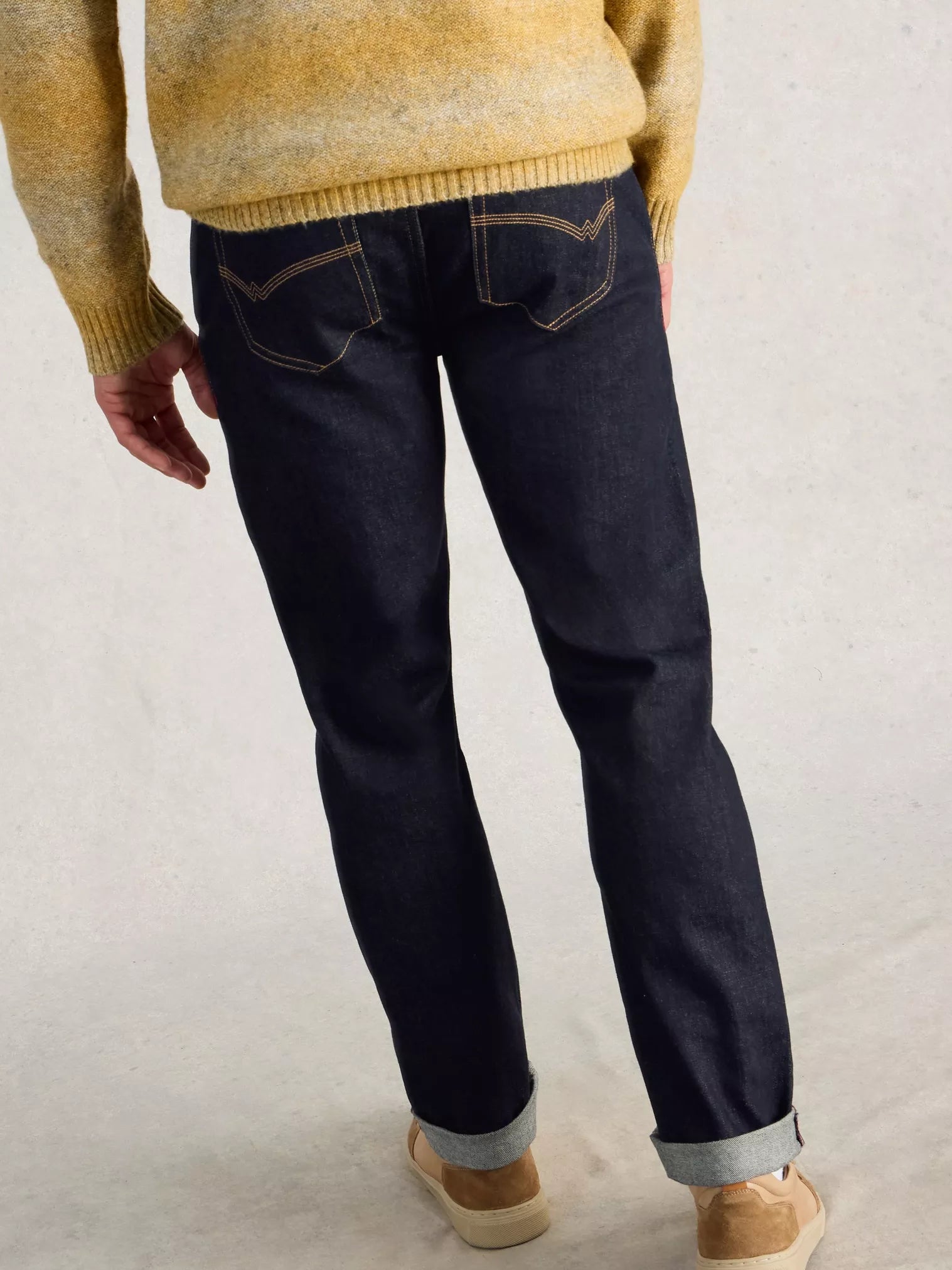 Person wearing dark blue jeans and a yellow sweater on a plain background