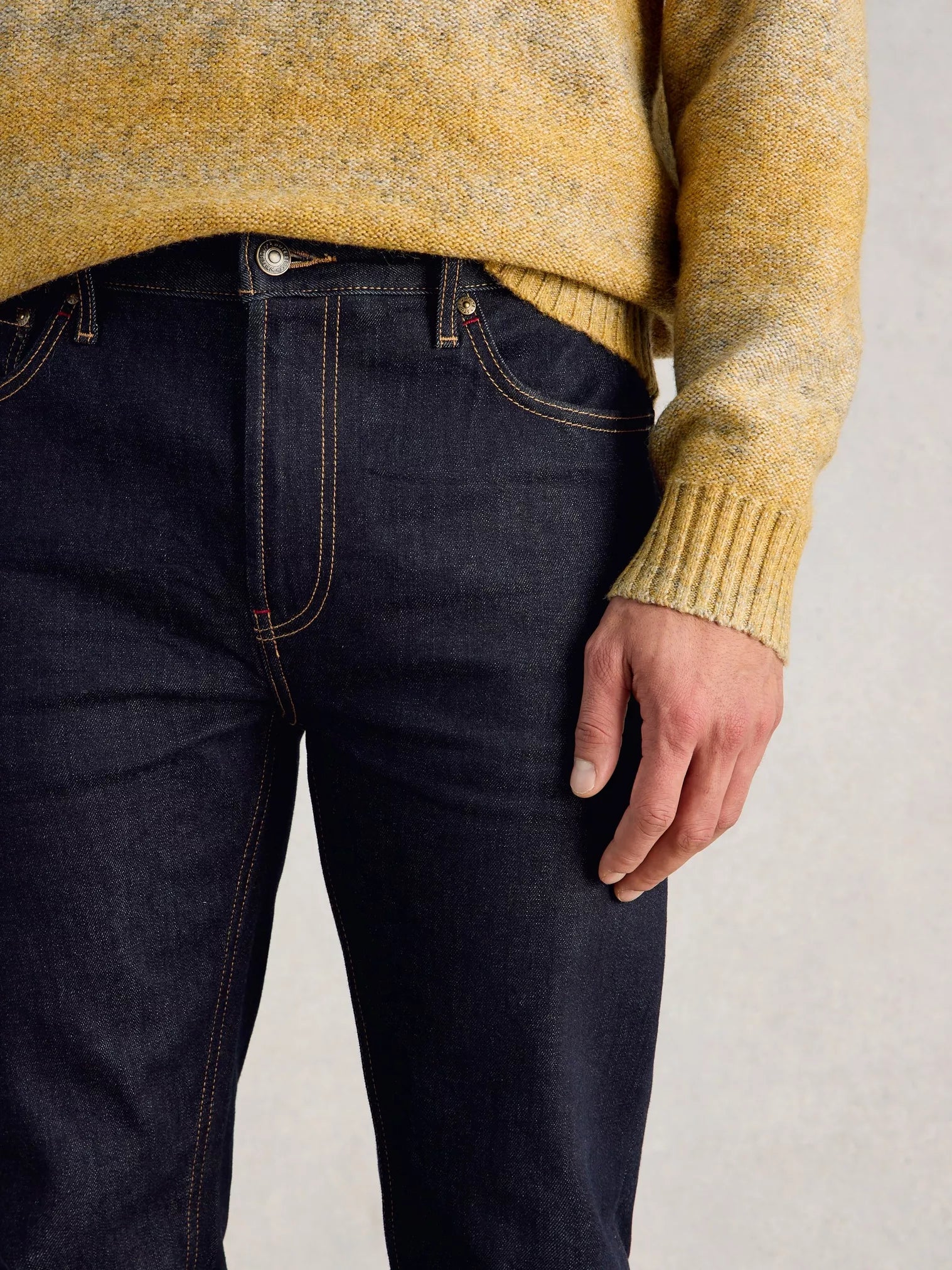 Person wearing a mustard yellow sweater and dark blue jeans on a light gray background