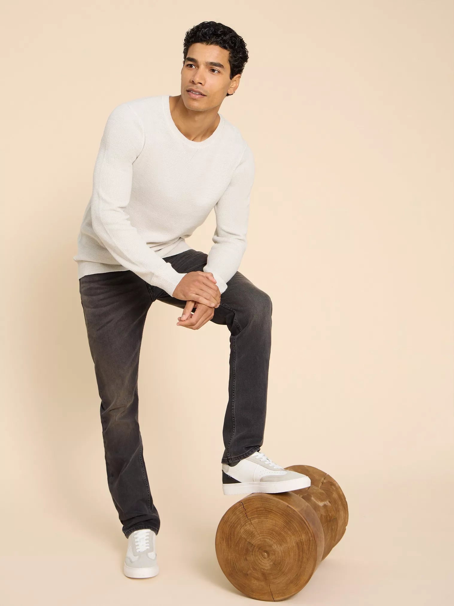 Cream-colored crewneck sweater and dark gray jeans; model wearing white and black sneakers.