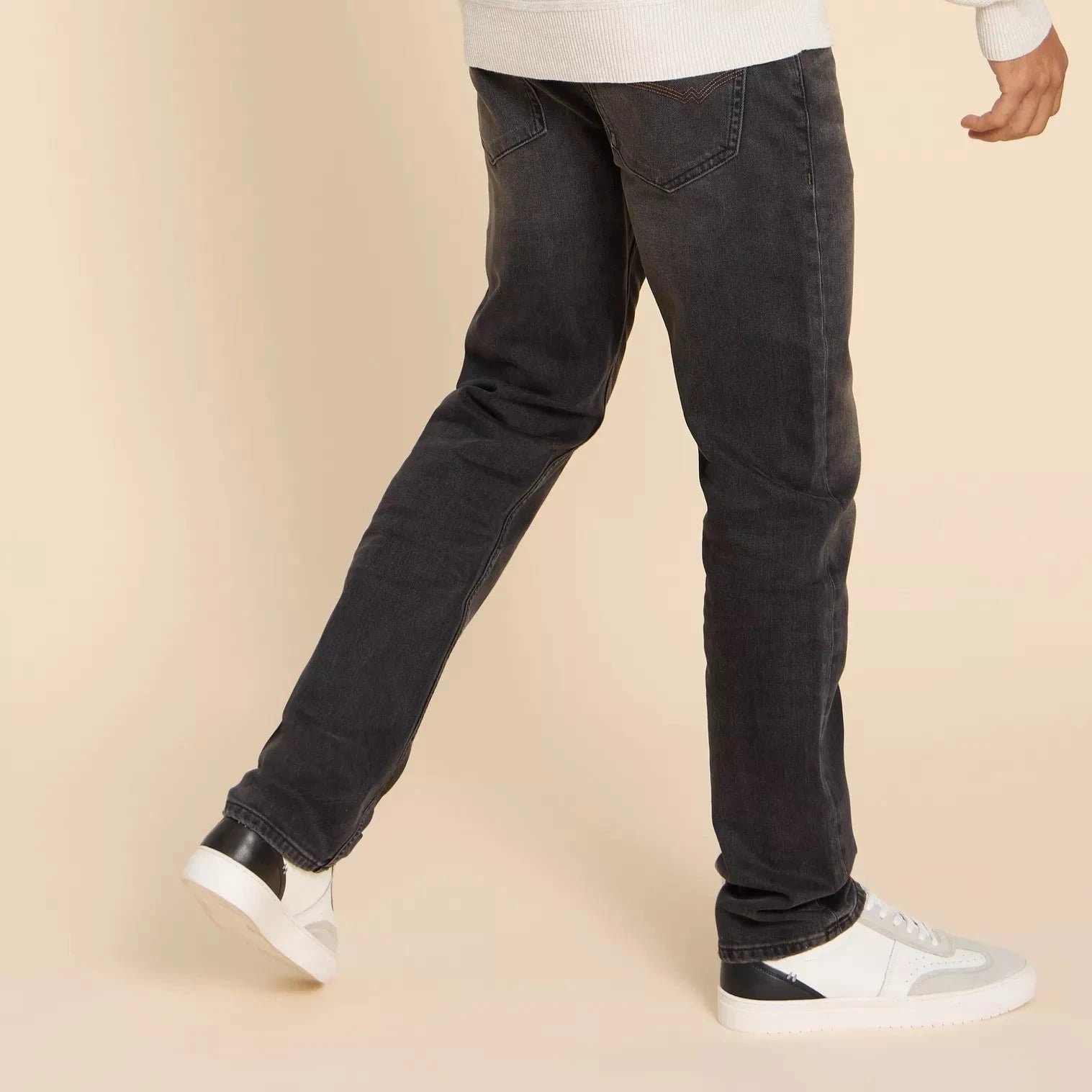 Dark gray straight-leg jeans shown from the knees down, with a person wearing white and black sneakers.