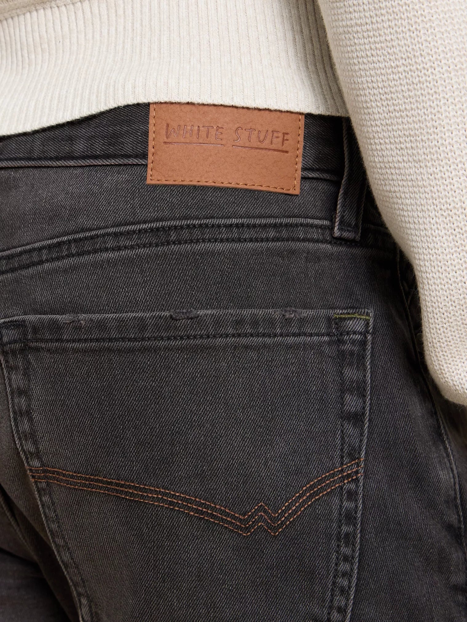 Dark gray denim jeans back pocket detail featuring a brown leather "White Stuff" label.